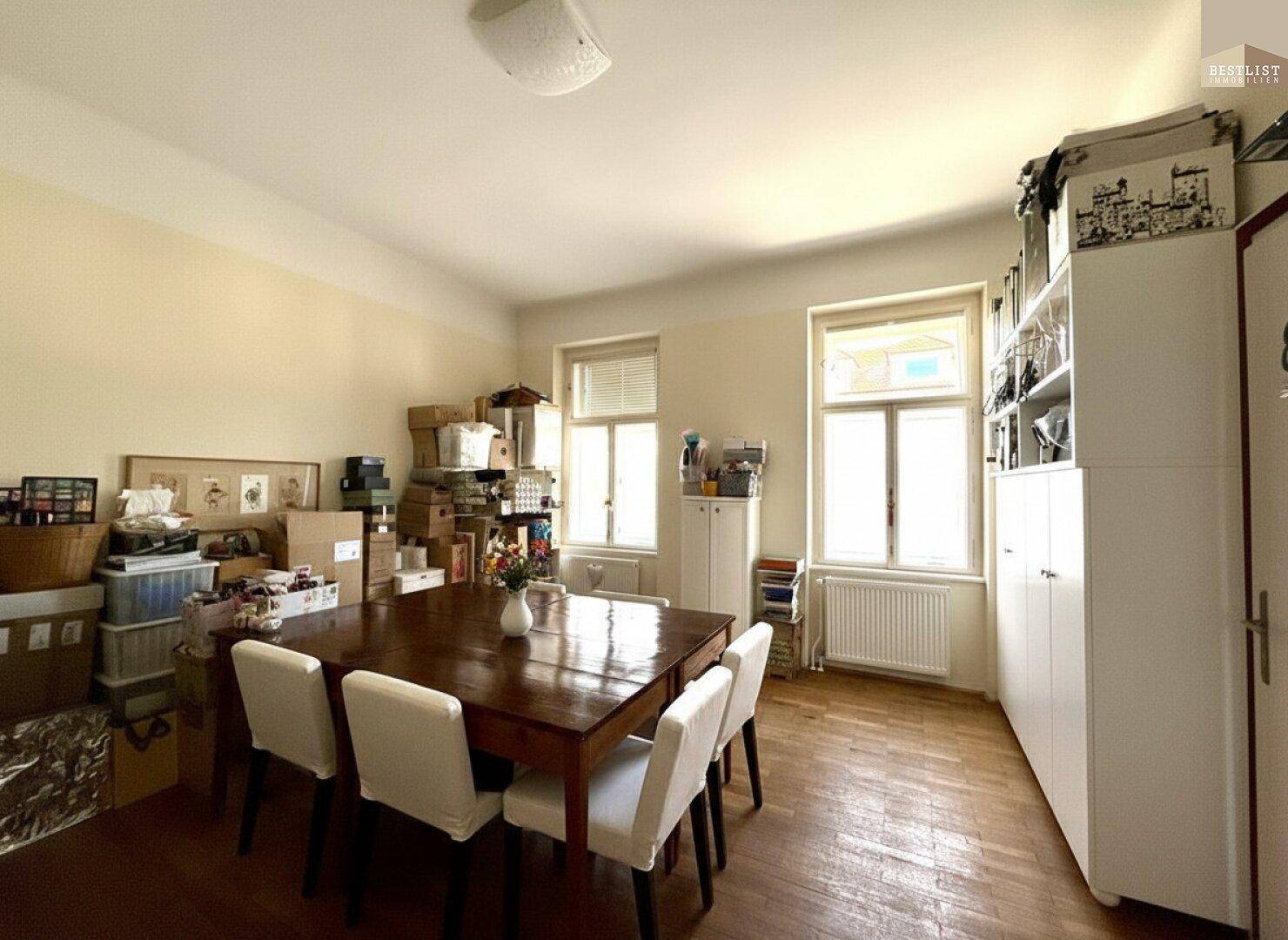 Geräumiges Esszimmer mit Holztisch, Stühlen und Fenstern, derzeit als Lagerraum genutzt.