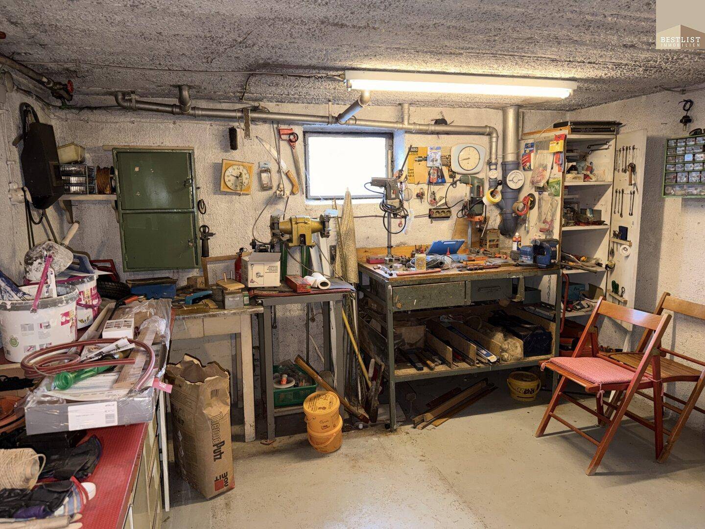 Werkstatt im Keller mit Arbeitsflächen, Werkzeugen und kleinem Fenster für Tageslicht.