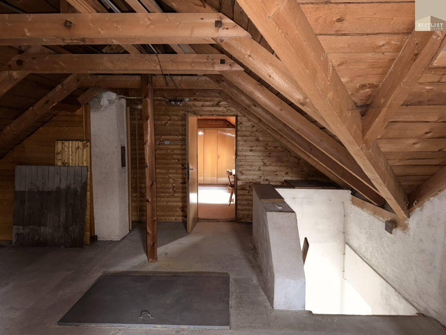 Unausgebauter Dachboden mit sichtbaren Holzbalken und Zugang zu weiteren Räumen.