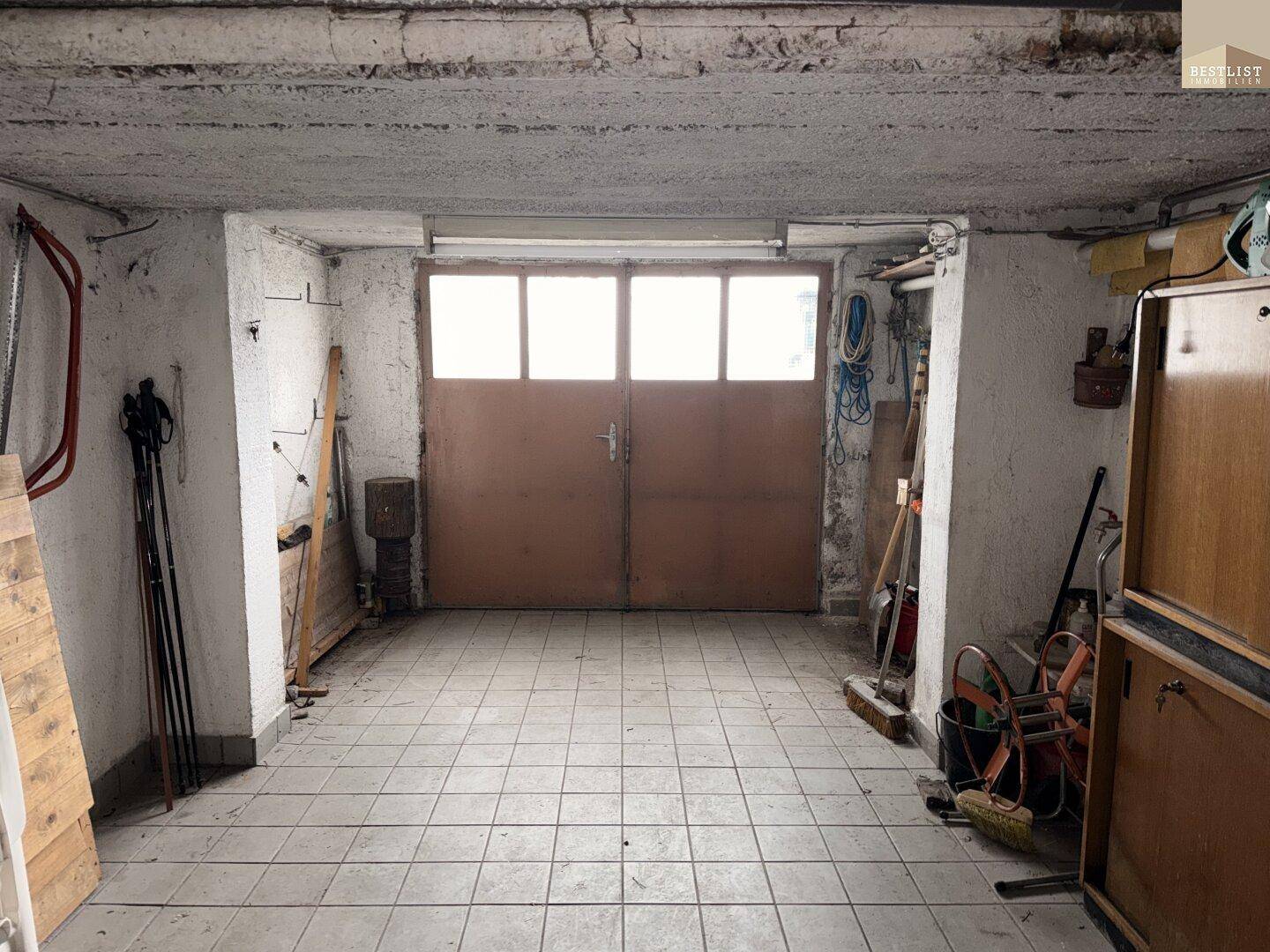 Geräumige Garage mit Fliesenboden und großem Tor für Fahrzeuge im Untergeschoss.