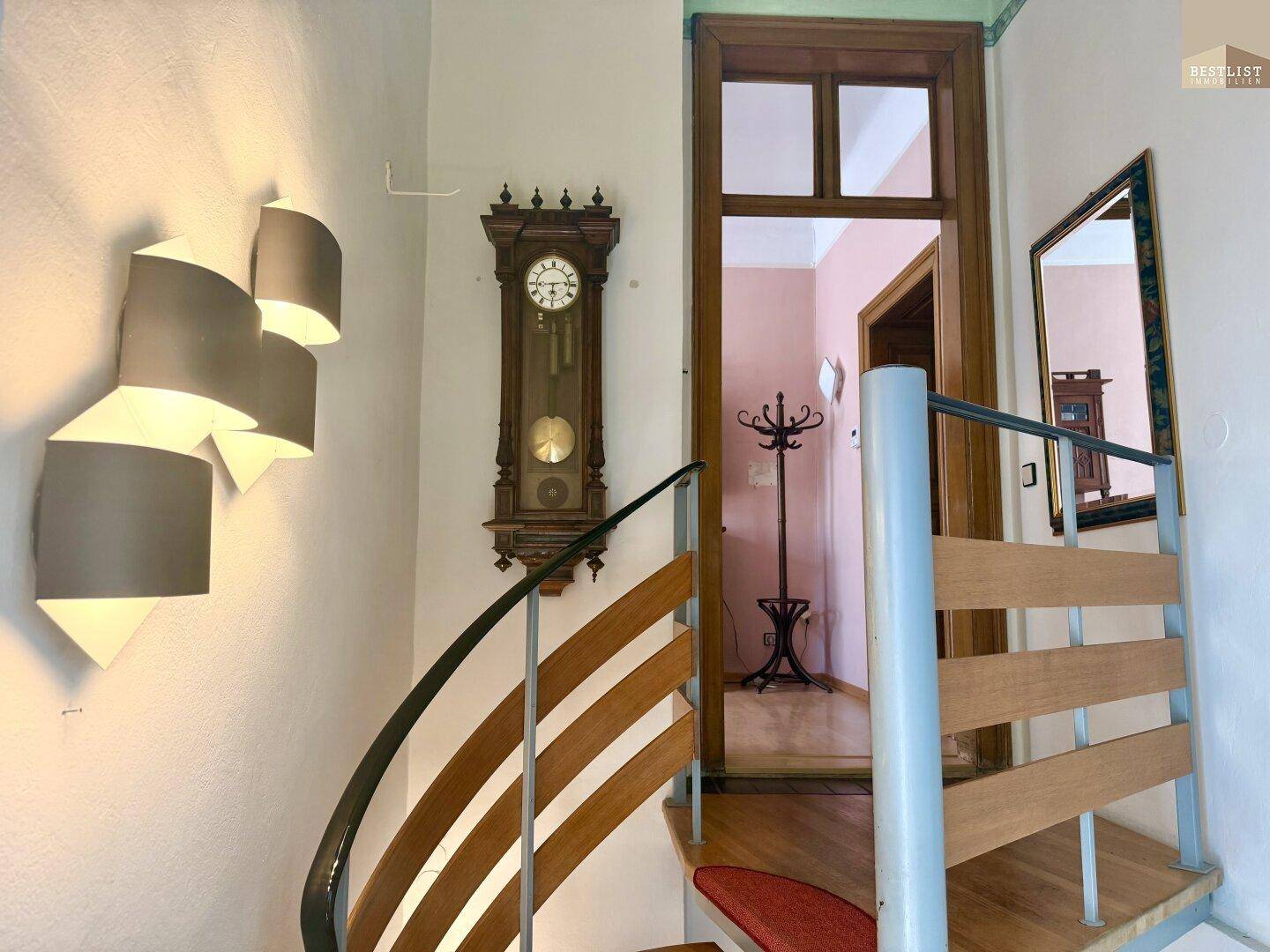 Wendeltreppe mit Holzstufen und Metallgeländer in einem hellen Flurbereich.