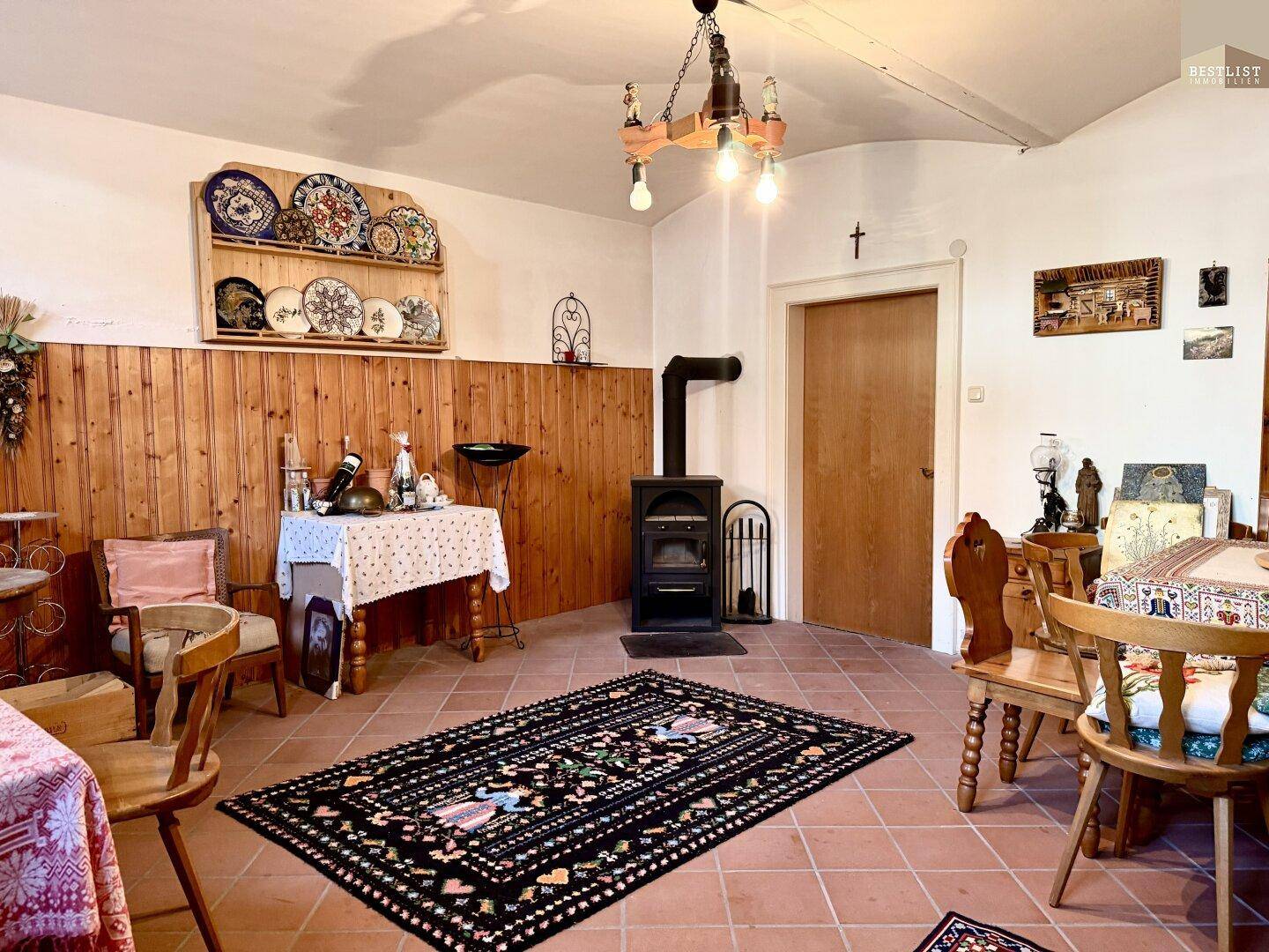Rustikaler Wohn-Essbereich mit Terrakottafliesen, Holzvertäfelung und einem Kaminofen.