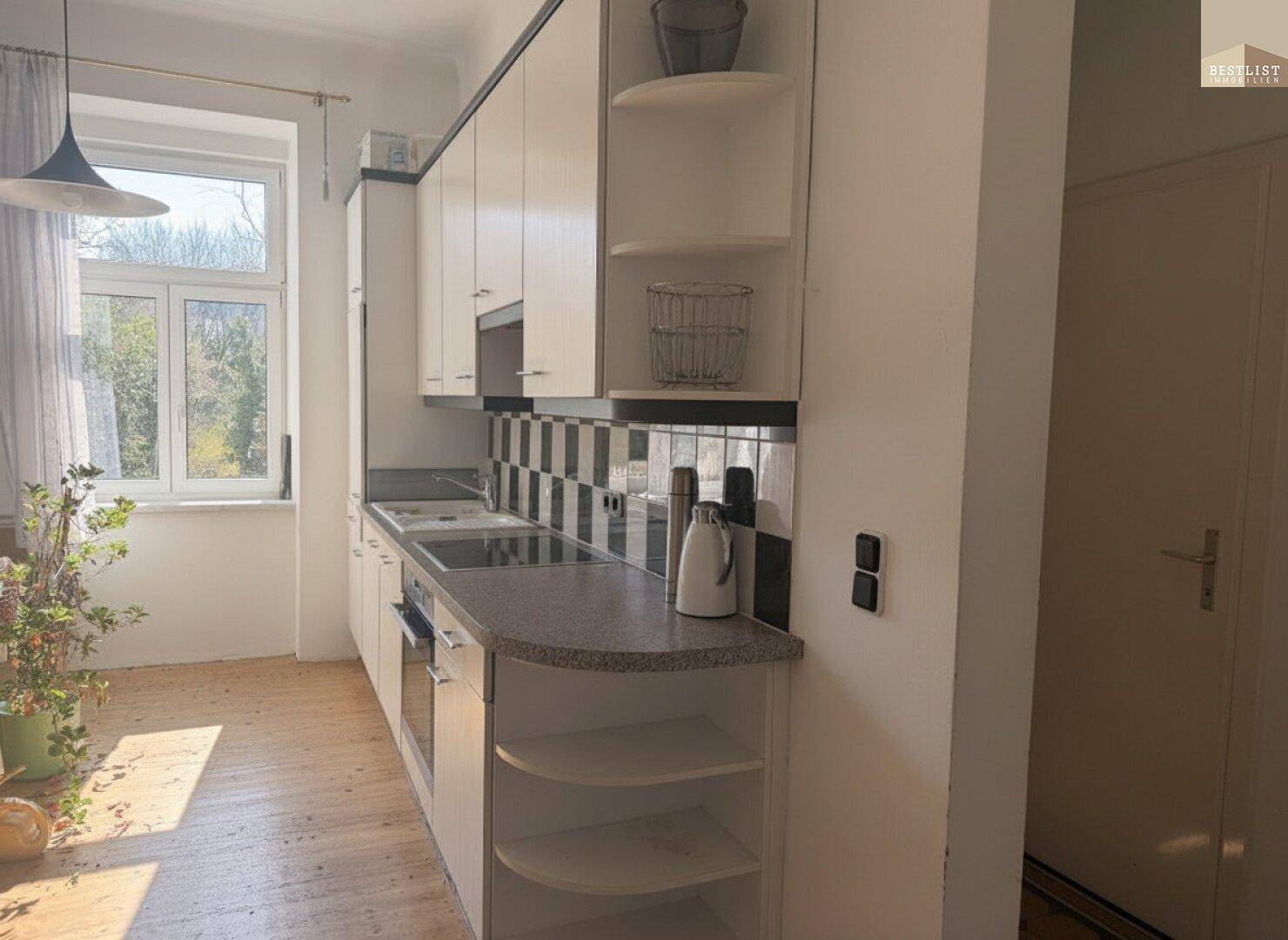 Küche mit weißen Schränken, Granitarbeitsplatte und kariertem Fliesenspiegel, hell durch ein Fenster.