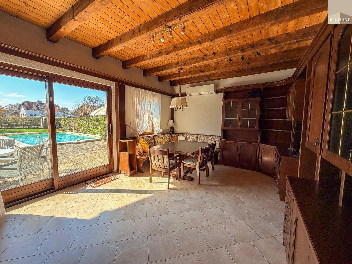 Gemütlicher Wohn-Essbereich mit Holzbalkendecke, Fliesenboden und Zugang zur Terrasse mit Poolblick.