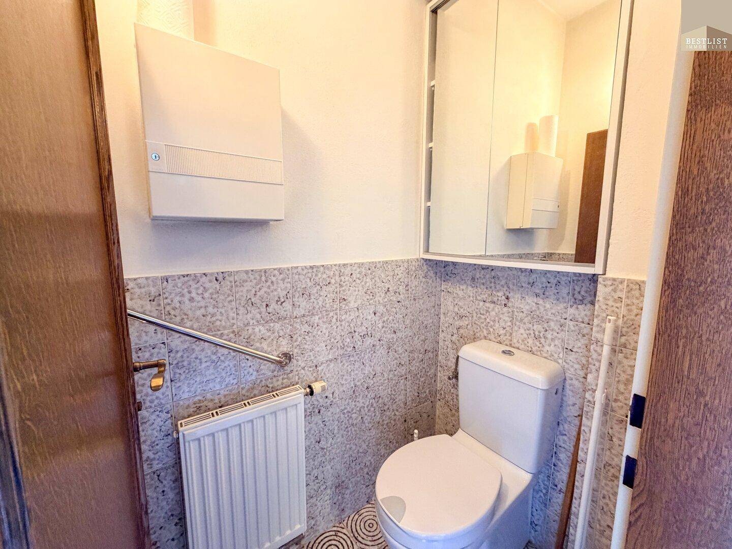 Separates WC mit Wandfliesen, Heizkörper und Spiegelschrank für Gäste.
