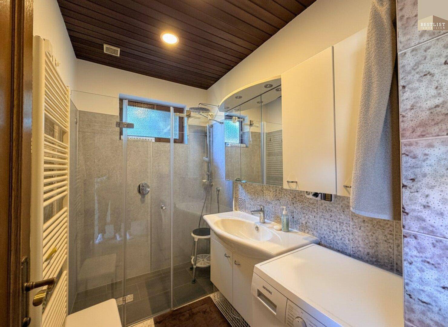 Modernes Badezimmer mit Dusche, Waschbecken und Holzdecke, gut beleuchtet.