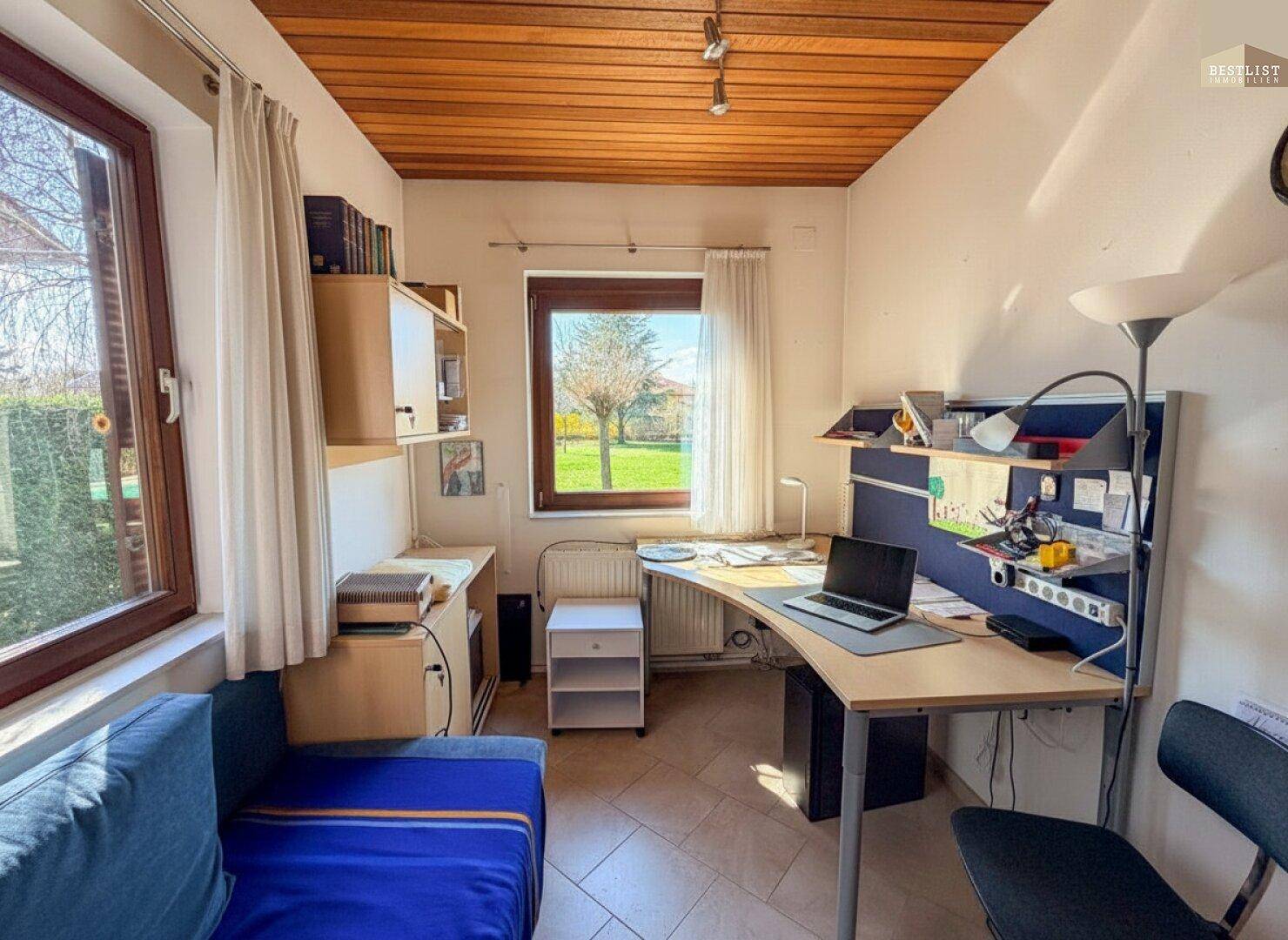 Funktionales Arbeitszimmer mit Schreibtisch, Stauraum und Blick in den grünen Gartenbereich.
