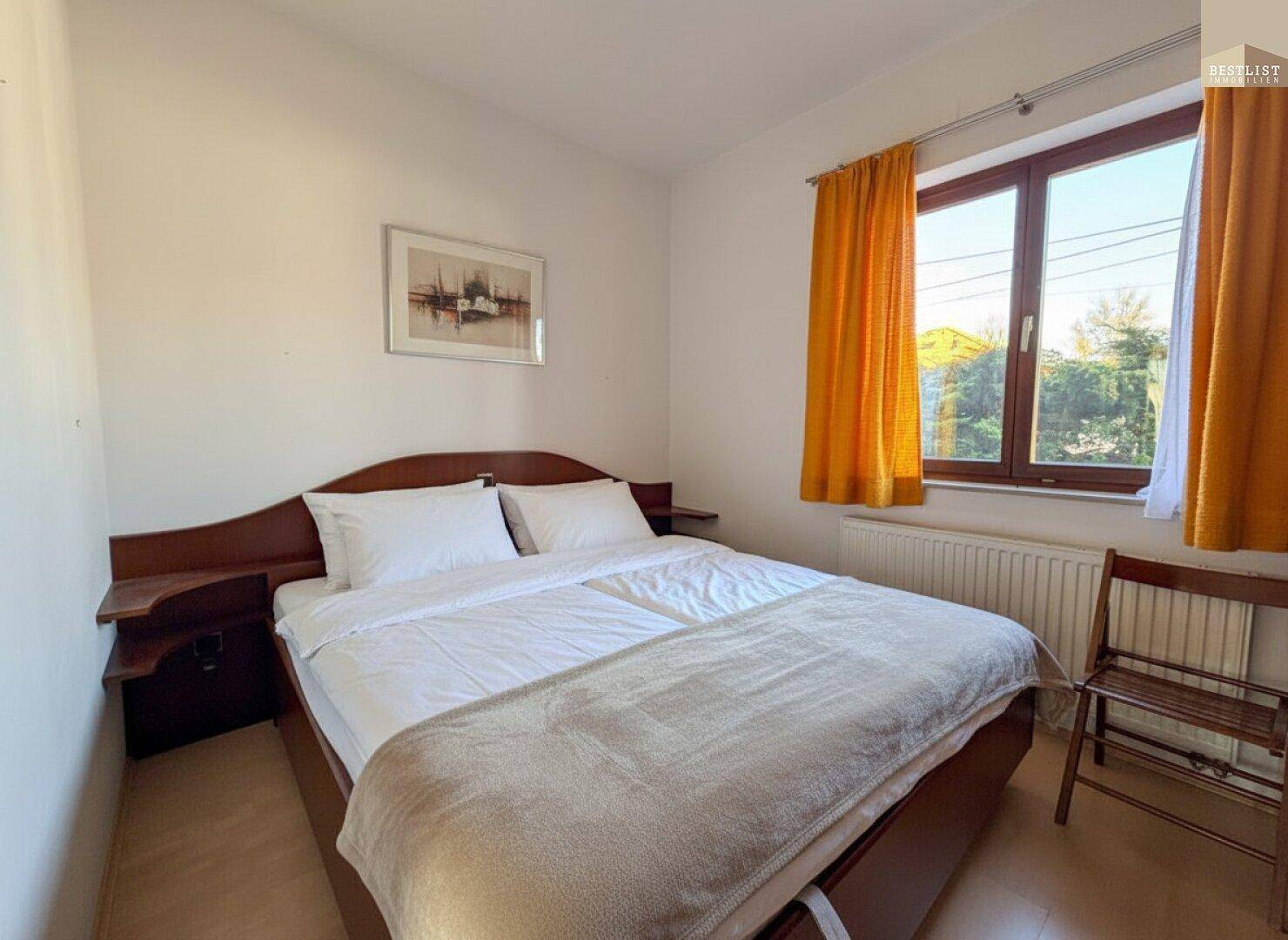 Helles Schlafzimmer mit Doppelbett, Holzmöbeln und großem Fenster für viel Tageslicht.