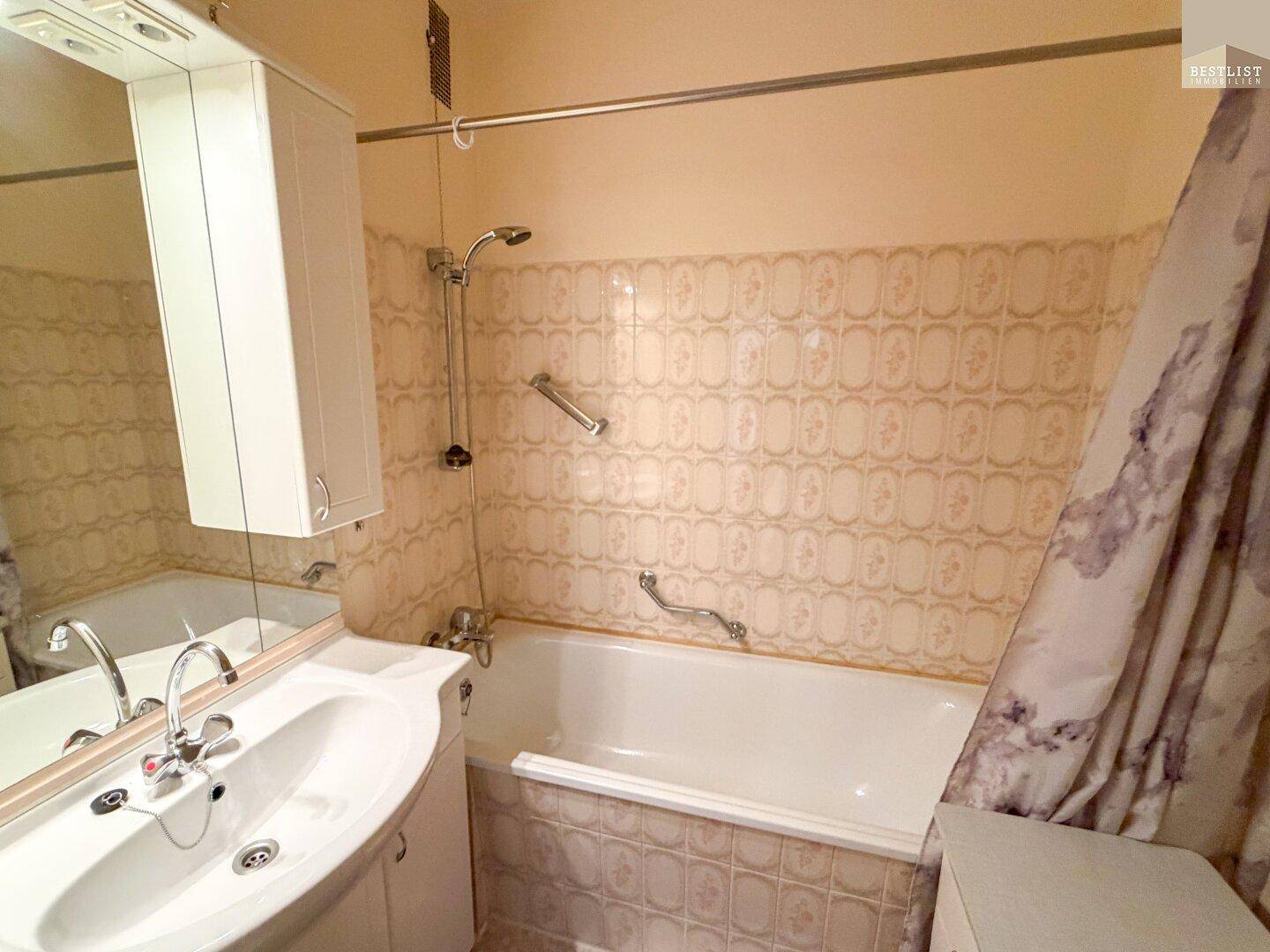 Badezimmer mit Badewanne, Duschfunktion, Waschbecken und gemusterten Fliesen im Retro-Stil.