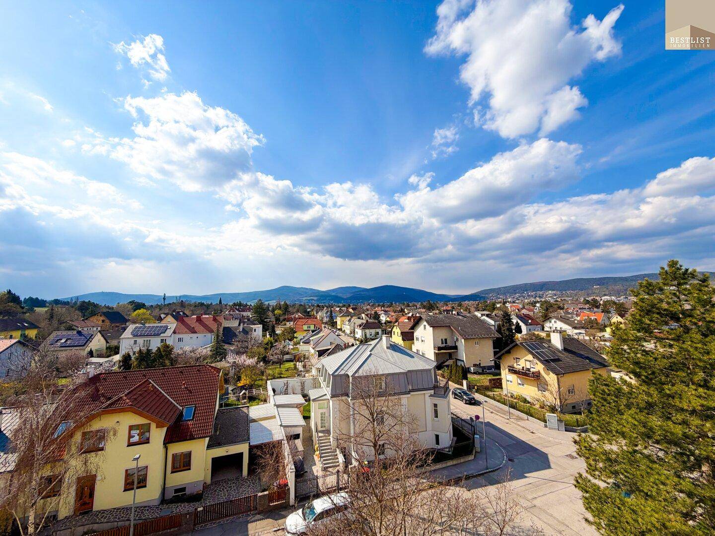 Weitläufiger Blick über eine Wohnsiedlung mit verschiedenen Häusern und einer Bergkette im Hintergrund.