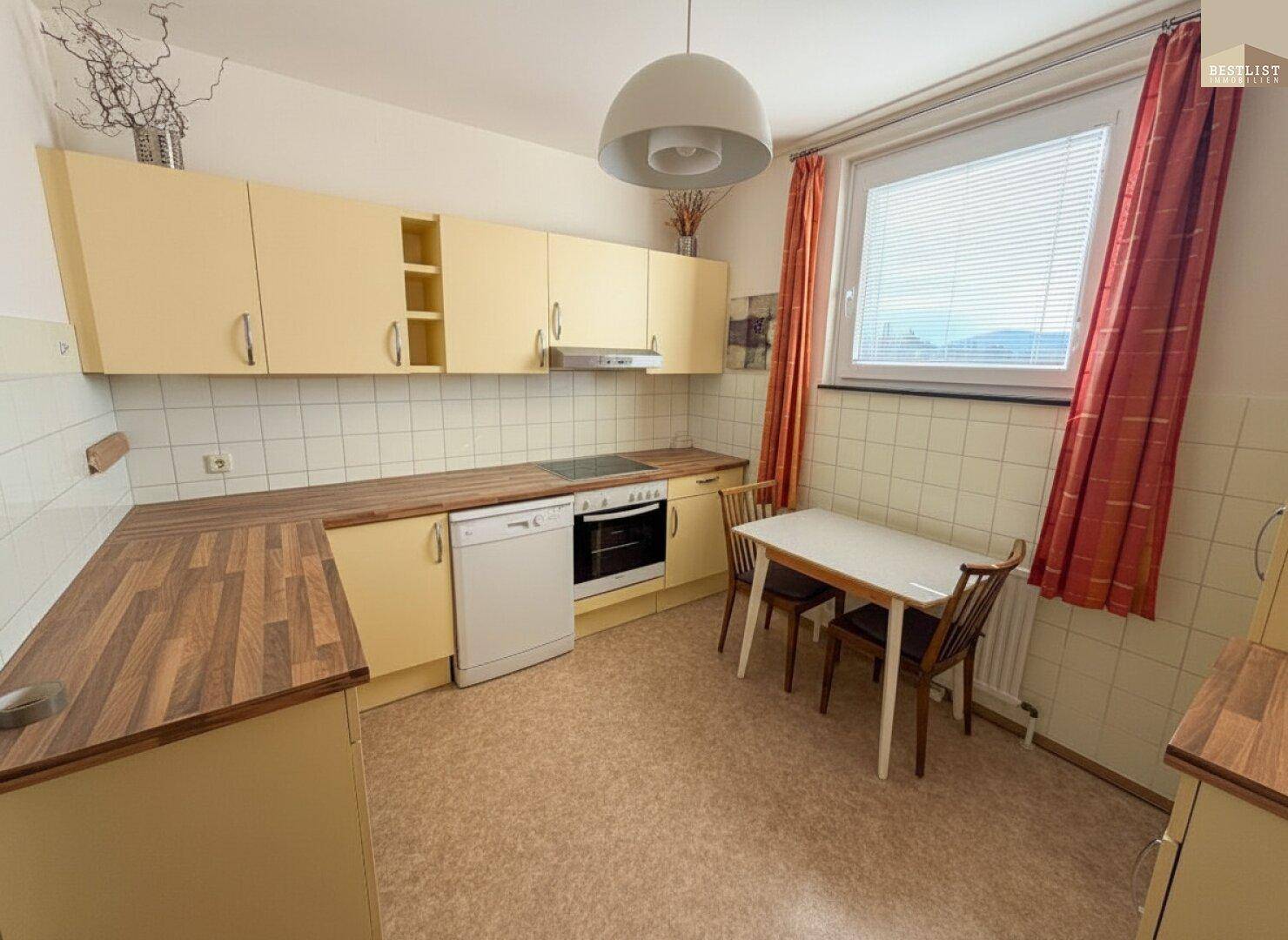 Küche mit gelben Einbauschränken, Holzarbeitsplatten und einem kleinen Essbereich am Fenster.