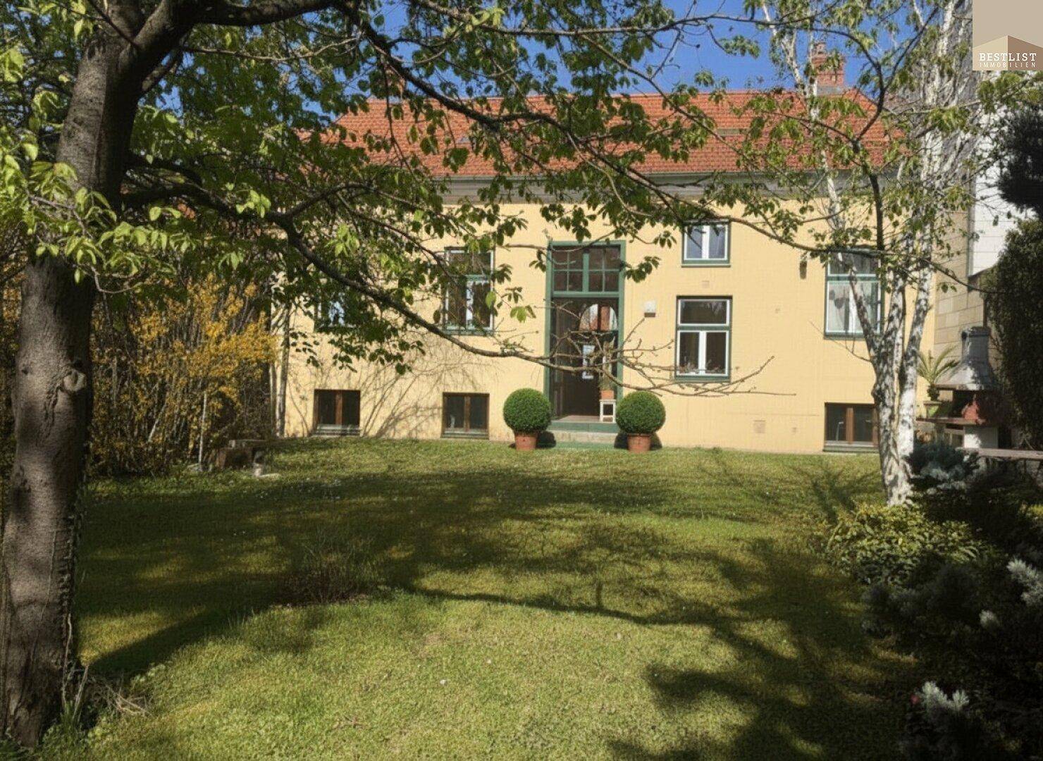 Rückansicht des Hauses mit großem Garten, Rasenfläche und Bäumen im Vordergrund.