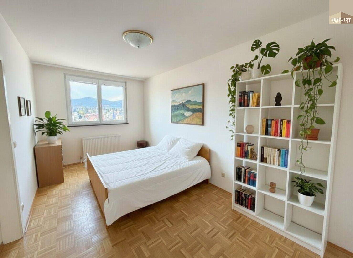 Gemütliches Schlafzimmer mit Parkettboden, Bett, Bücherregal und Blick aus dem Fenster.