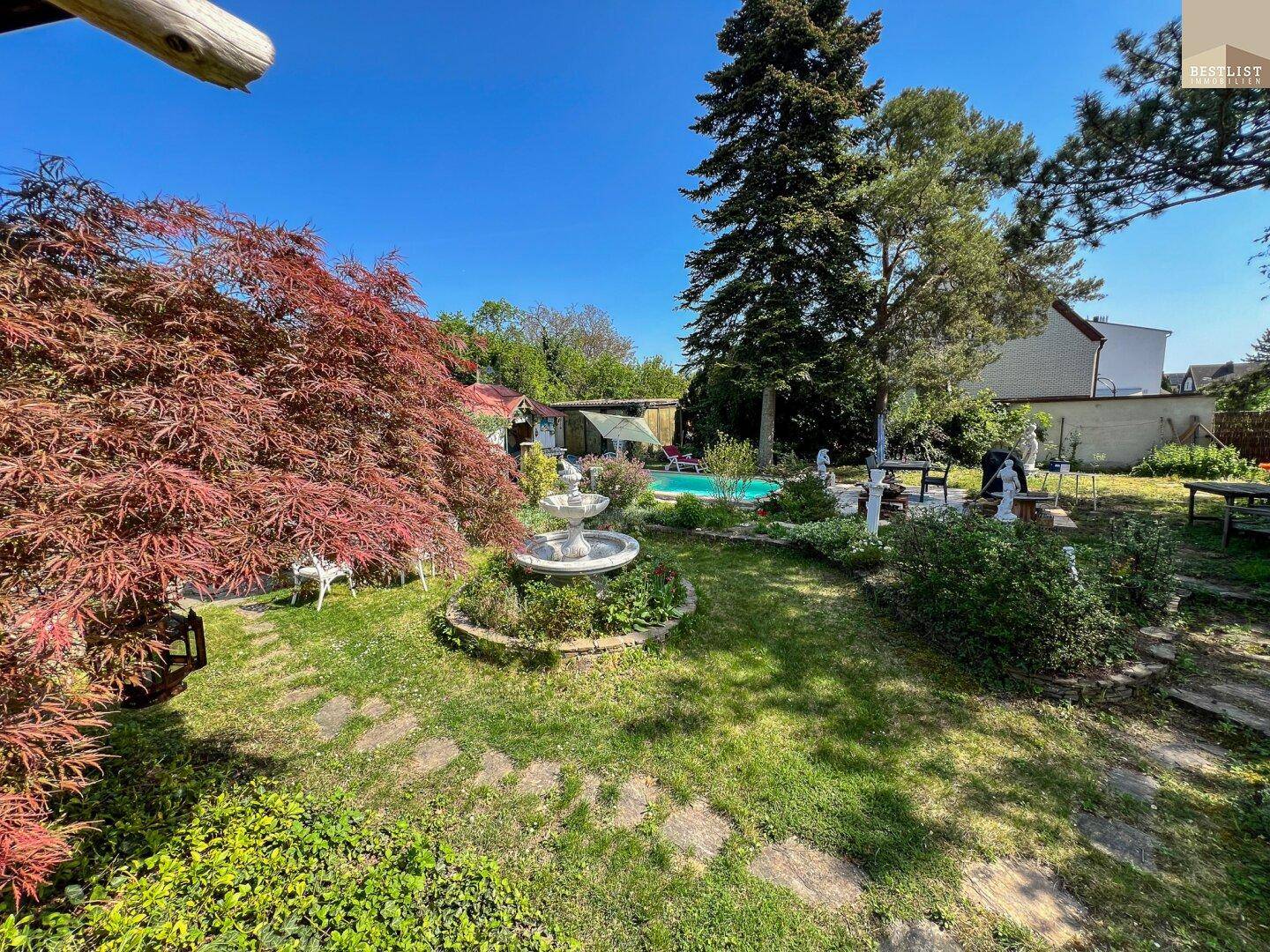Weitläufiger Garten mit Rasenfläche, Bäumen, Springbrunnen und Pool im Hintergrund.