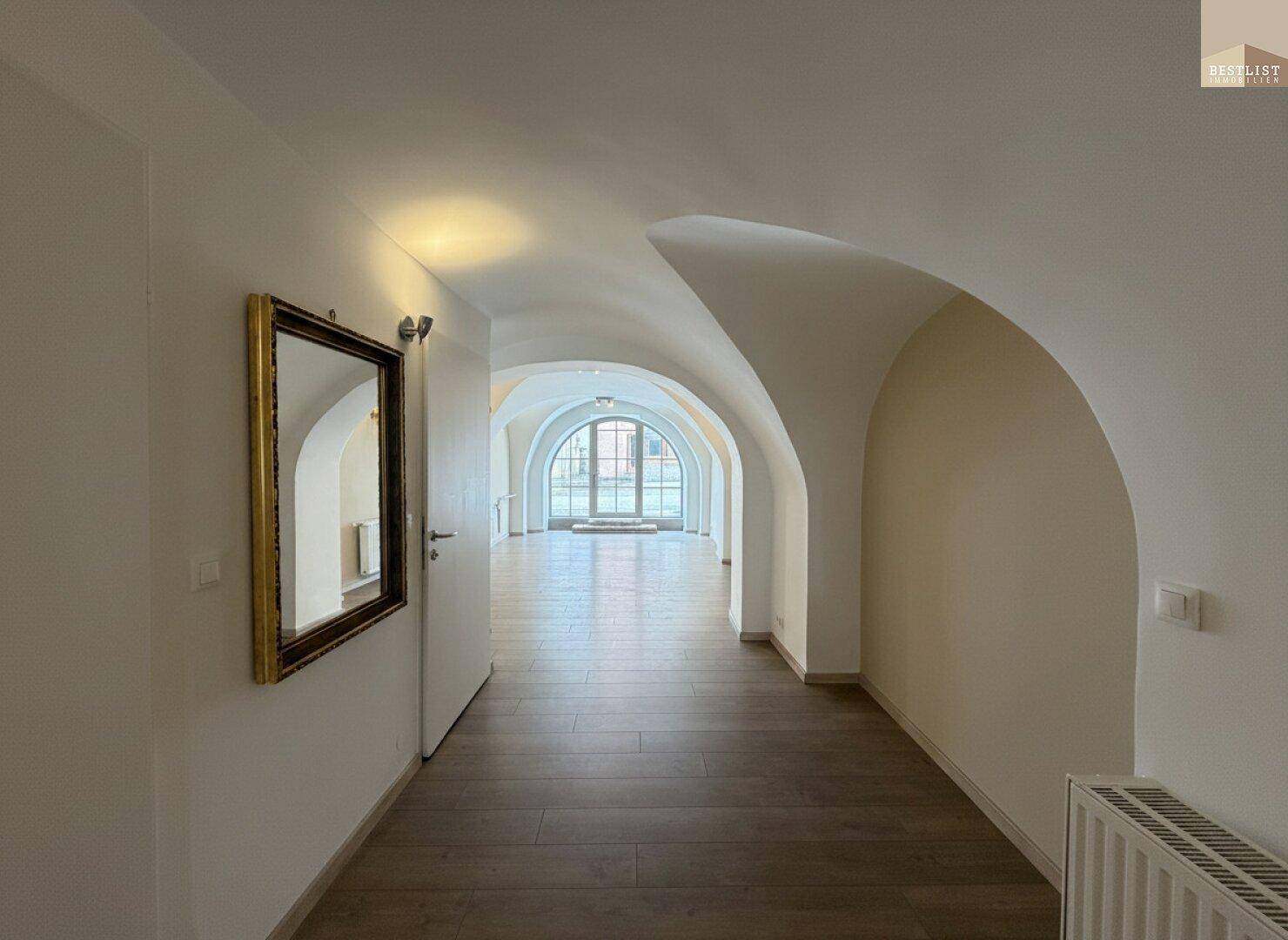 Heller Flur mit eleganten Gewölbedecken, Holzboden und einem dekorativen Spiegel.