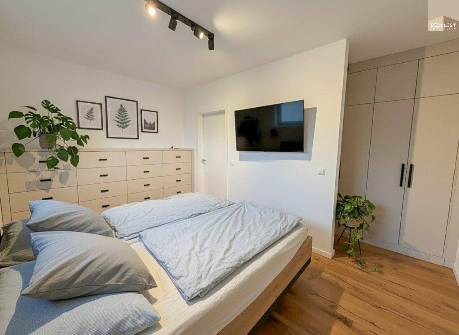 Helles Schlafzimmer mit Doppelbett, Kommode und integriertem Kleiderschrank.