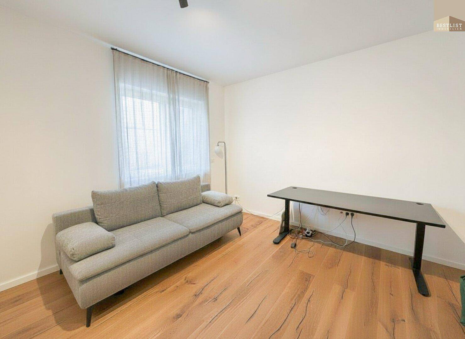Flexibler Raum mit Sofa und Schreibtisch, ideal als Büro oder Gästezimmer nutzbar.