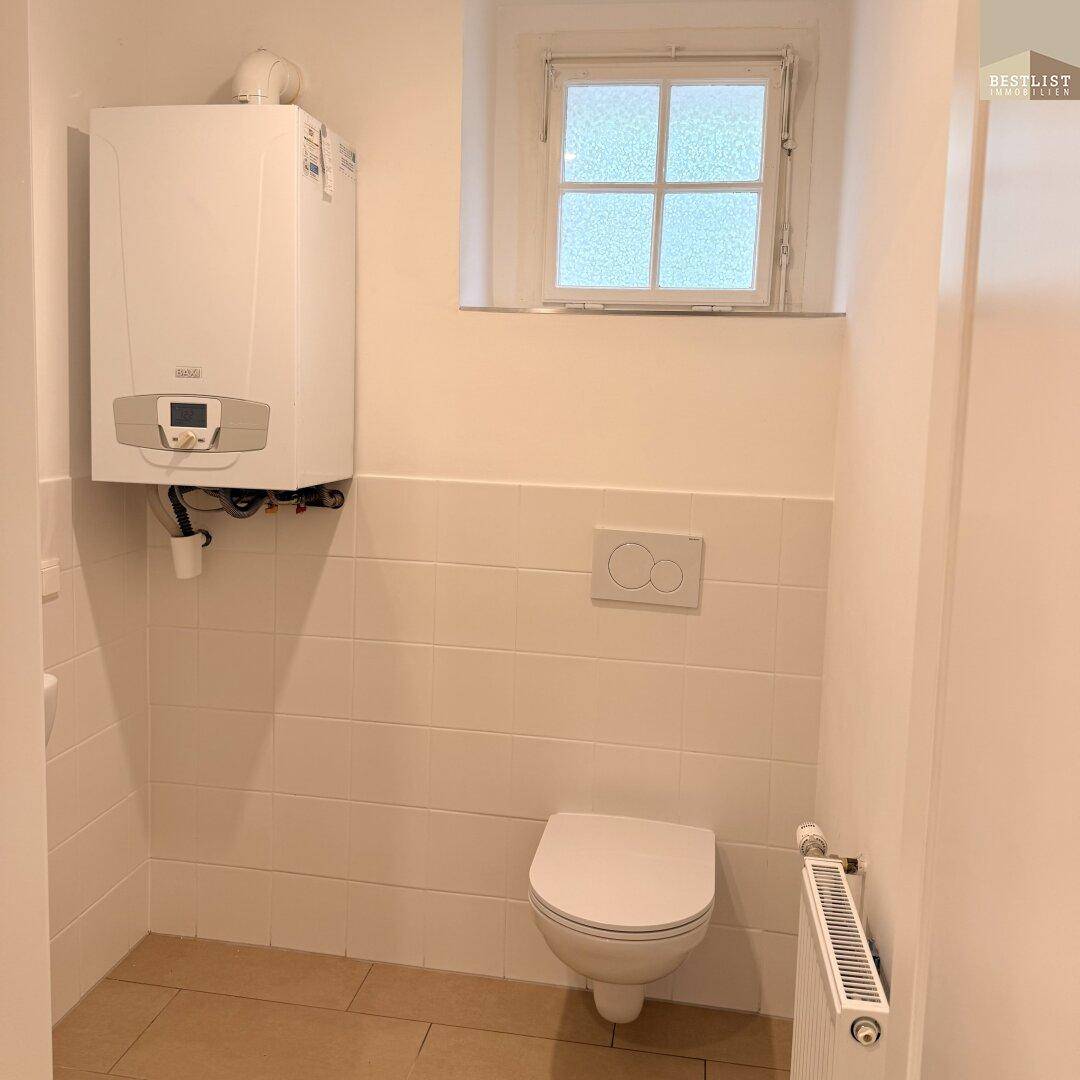 Kleiner Raum mit wandhängender Toilette, Heizungsanlage und einem kleinen Fenster.