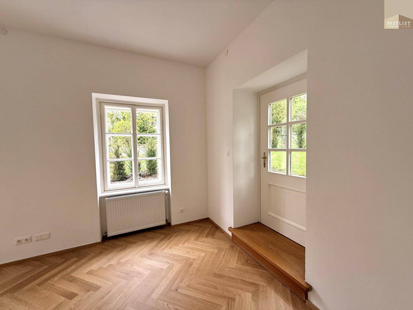 Heller Raum mit Fischgrätparkett und einem Fenster, das den Blick ins Grüne freigibt.