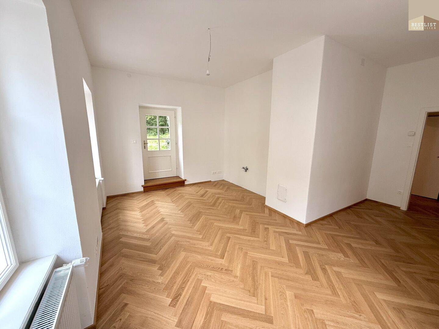 Geräumiger, heller Raum mit Fischgrätparkett und Fenstern, die viel Tageslicht hereinlassen.