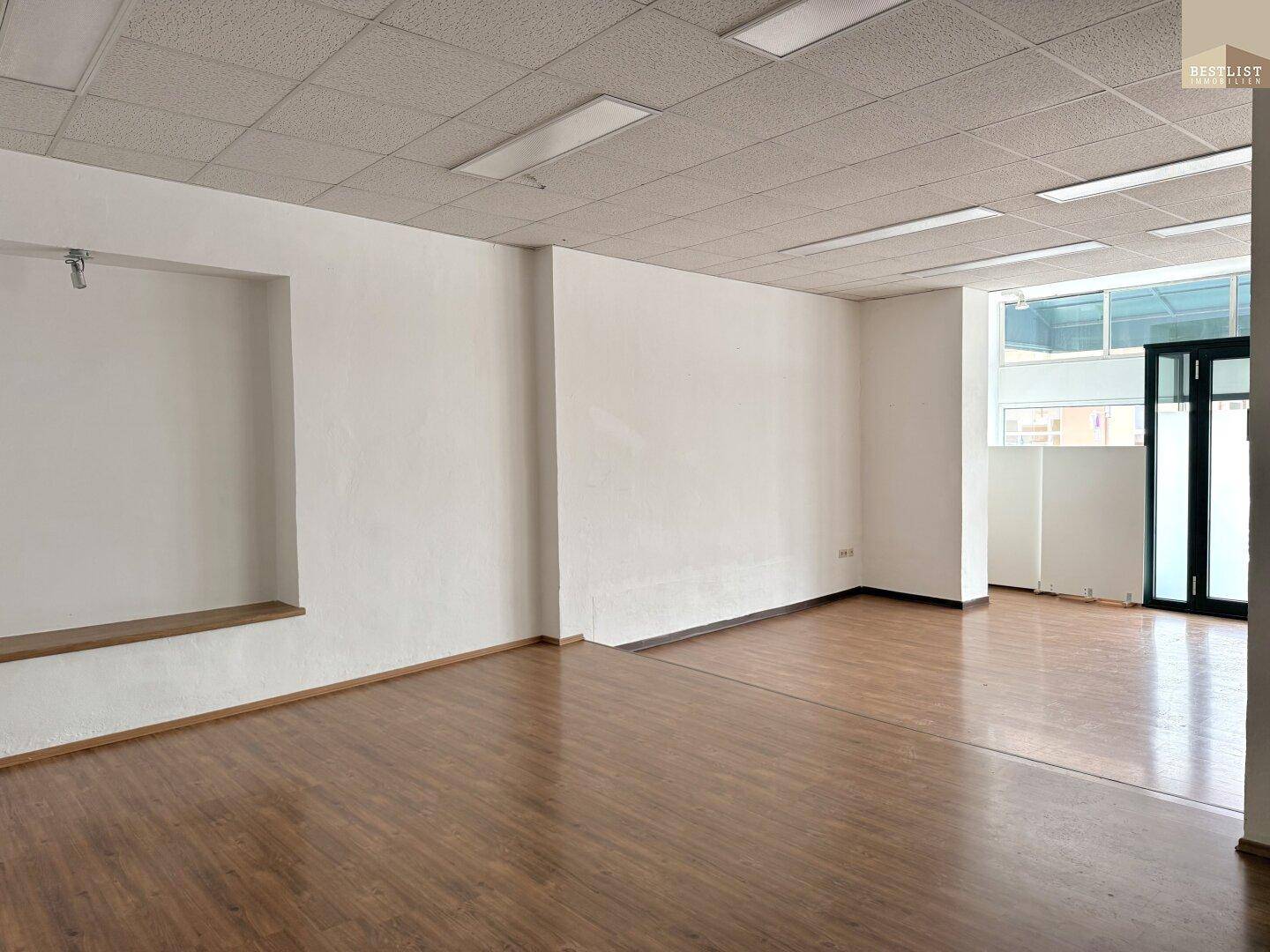 Geräumiger, leerer Büroraum mit Holzfußboden und viel Tageslicht durch die Fenster.