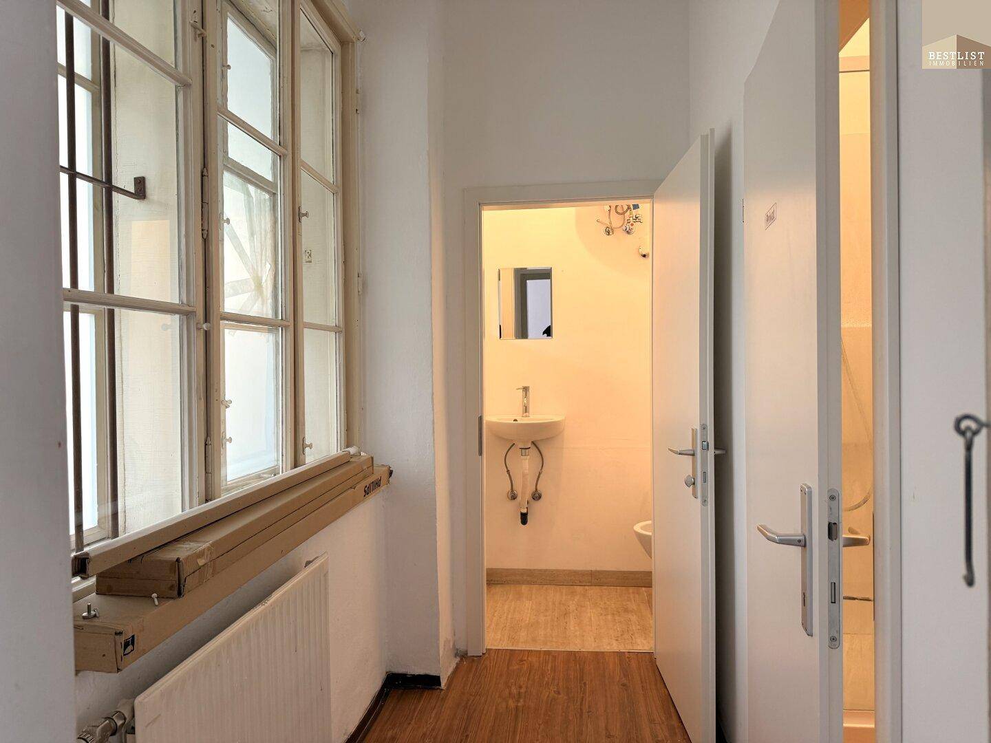 Flur mit Holzfußboden, der zu einem Badezimmer mit Waschbecken und Toilette führt.