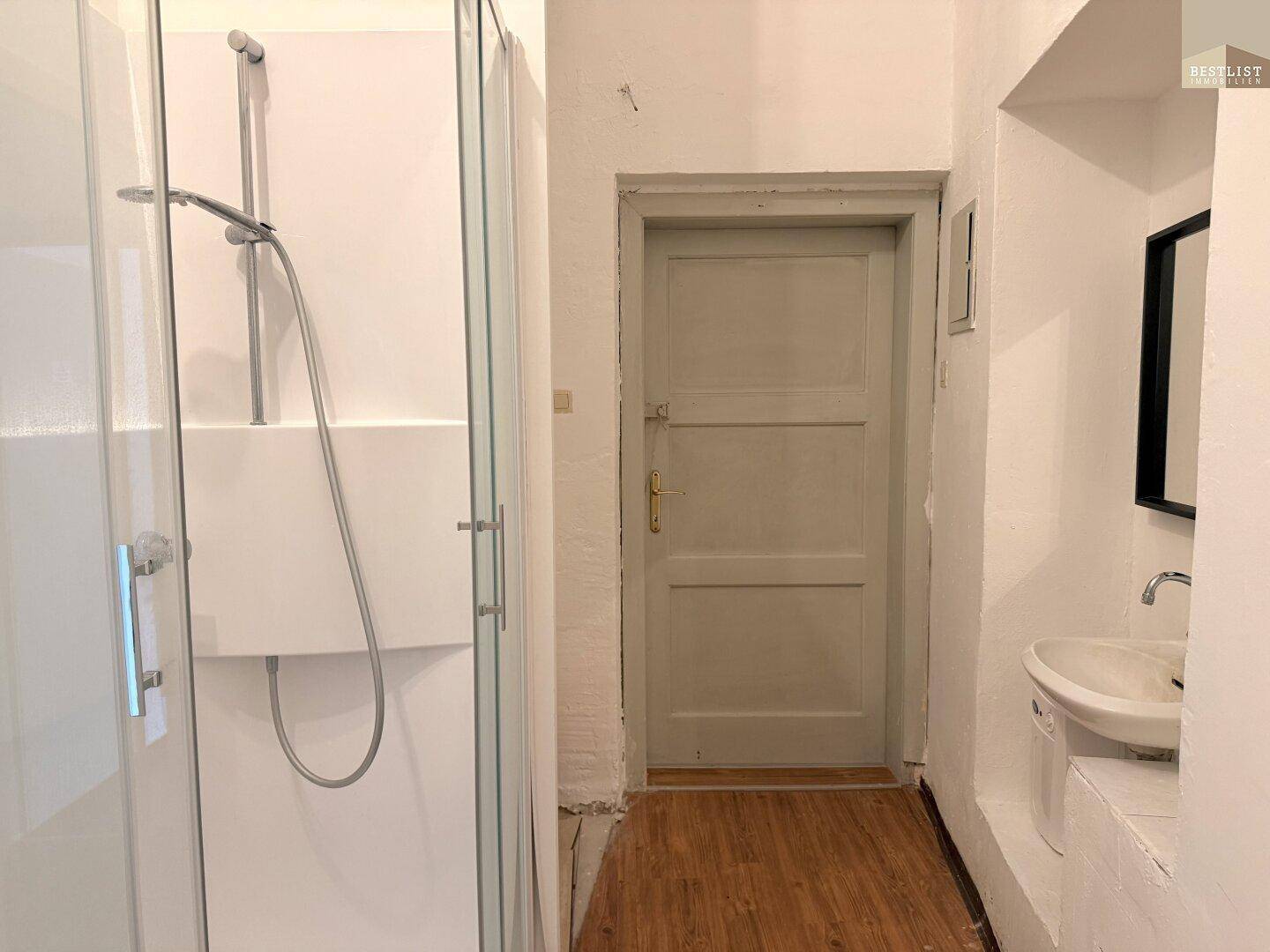 Badezimmer mit Duschkabine, Waschbecken und einer schlichten Holztür.