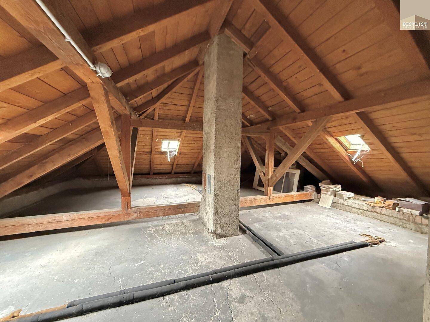 Unausgebauter Dachboden mit sichtbaren Holzbalken, Betonboden und Dachfenstern.