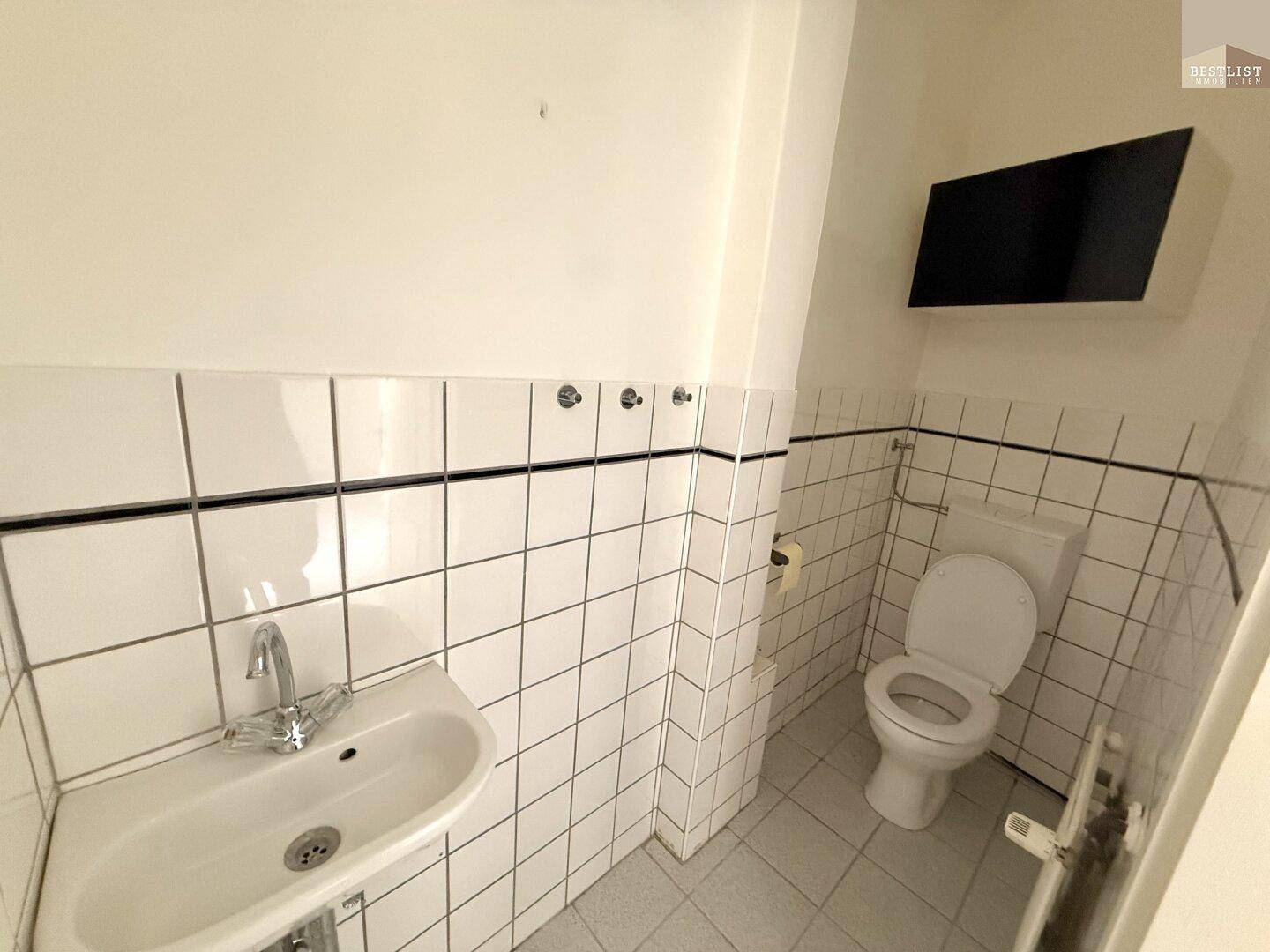 Kleines WC mit weißen Fliesen, Toilette und Waschbecken.