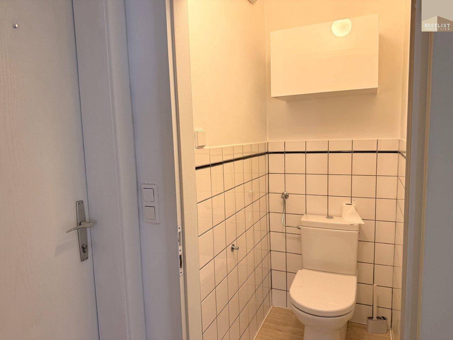 Modernes WC mit weißen Fliesen und einer Toilette.