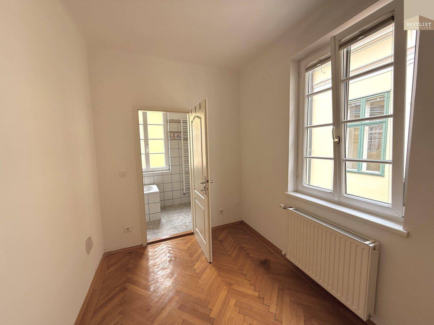 Zimmer mit Fischgrätparkett und direktem Zugang zu einem gefliesten Badezimmer.