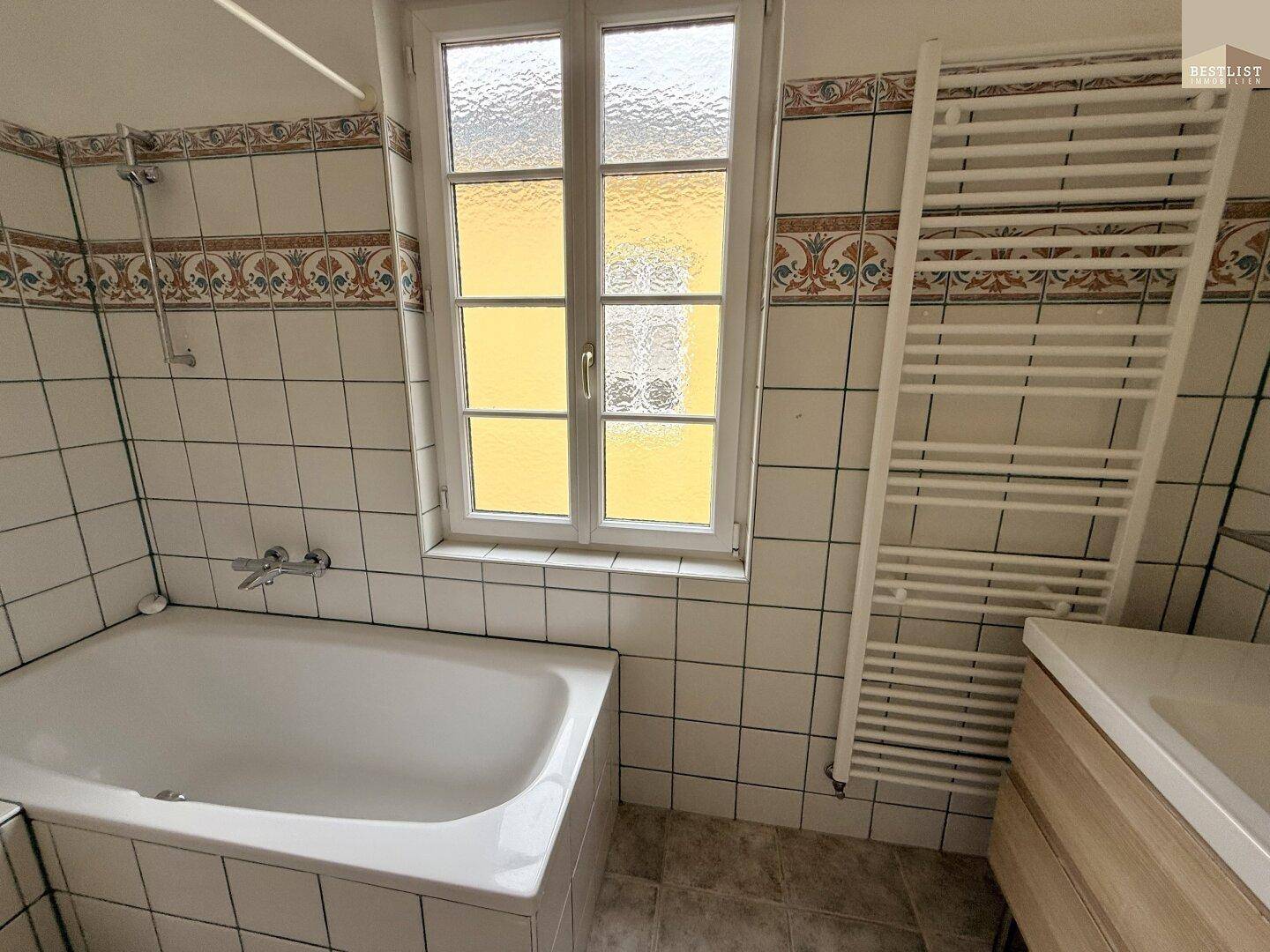 Badezimmer mit Badewanne, gefliesten Wänden und einem beheizten Handtuchhalter.