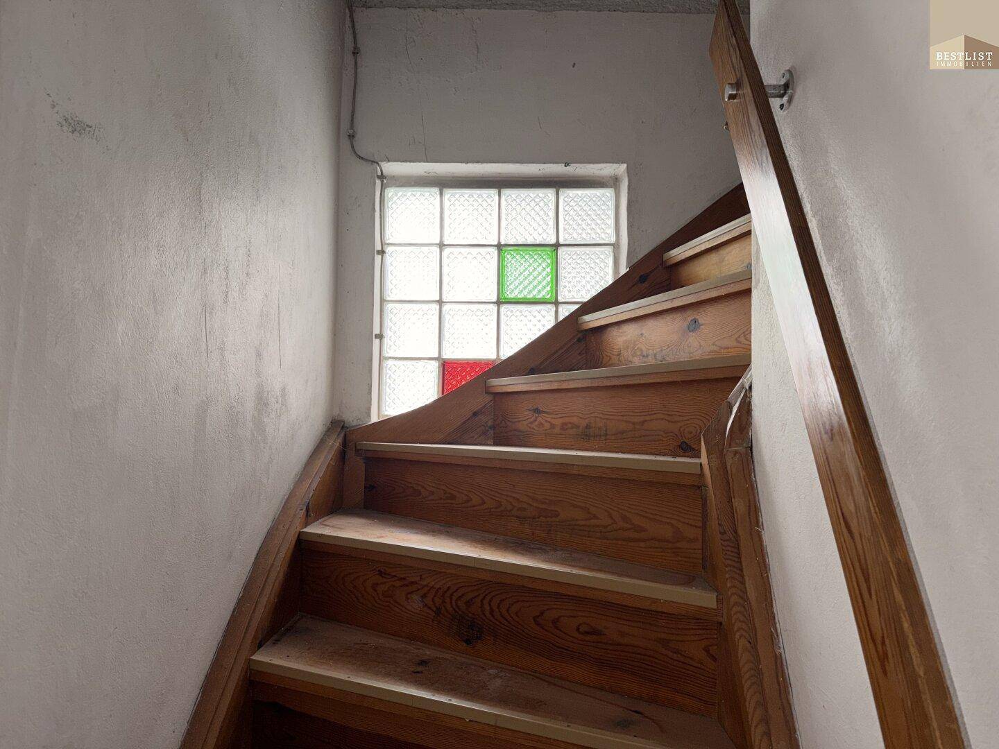 Holztreppe mit Handlauf und einem Fenster aus Glasbausteinen, das natürliches Licht spendet.