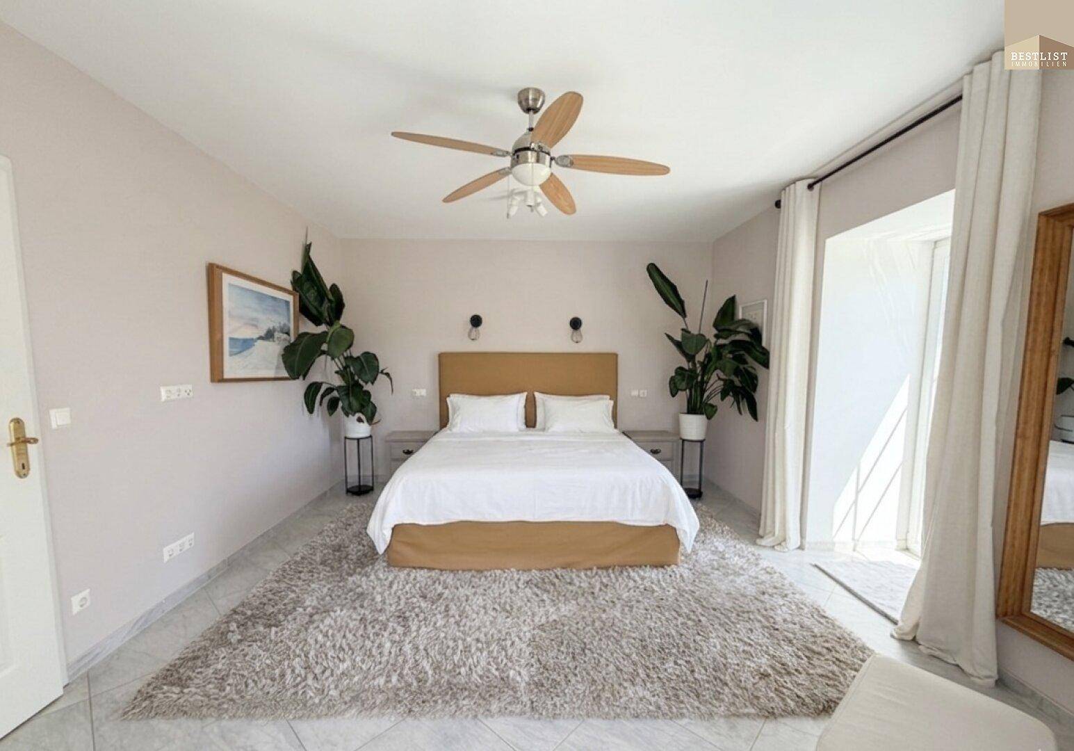 Helles Schlafzimmer mit Doppelbett, Fliesenboden und Zugang zu einem Balkon.
