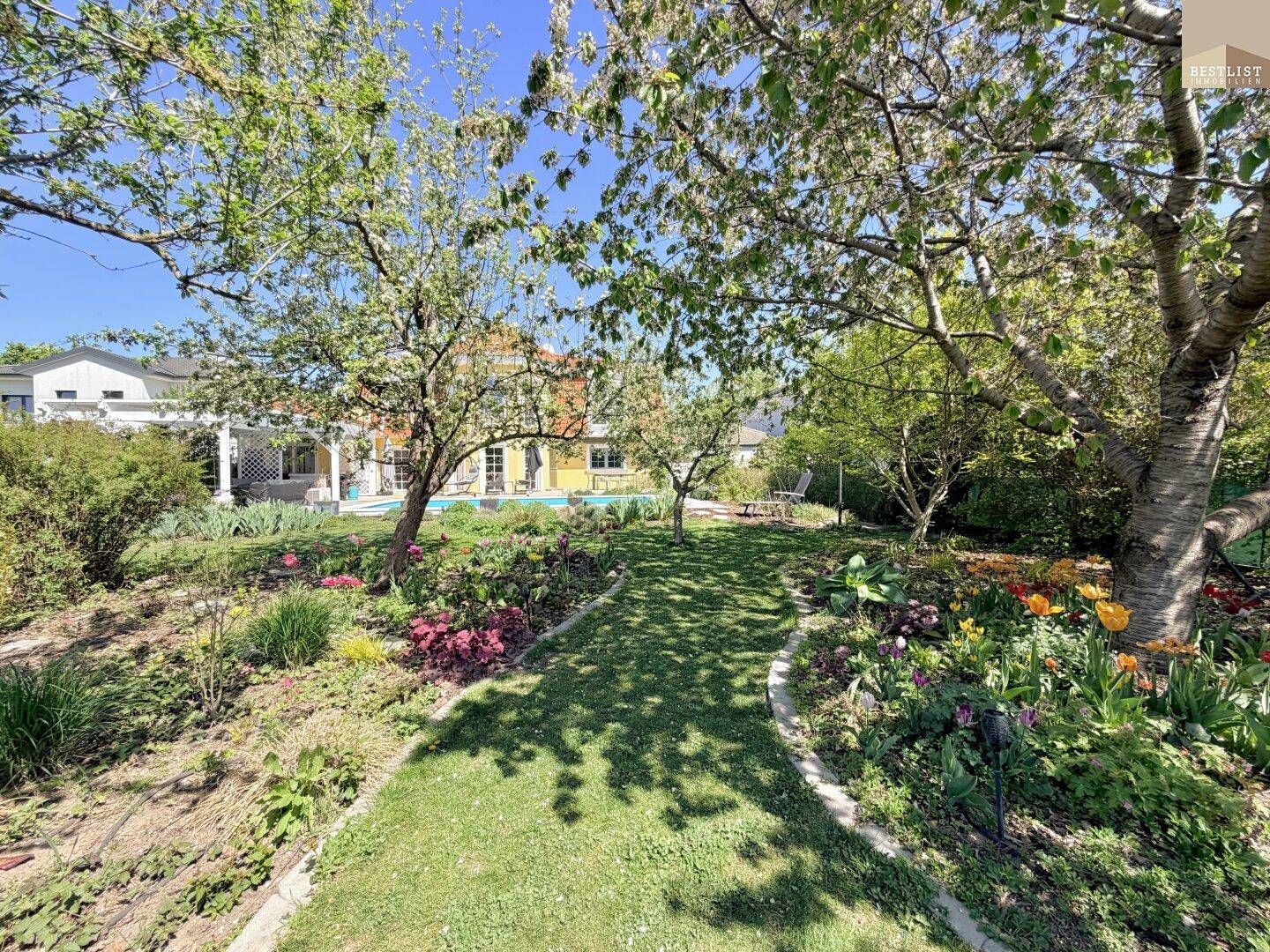 Gepflegter Garten mit blühenden Blumenbeeten und altem Baumbestand.
