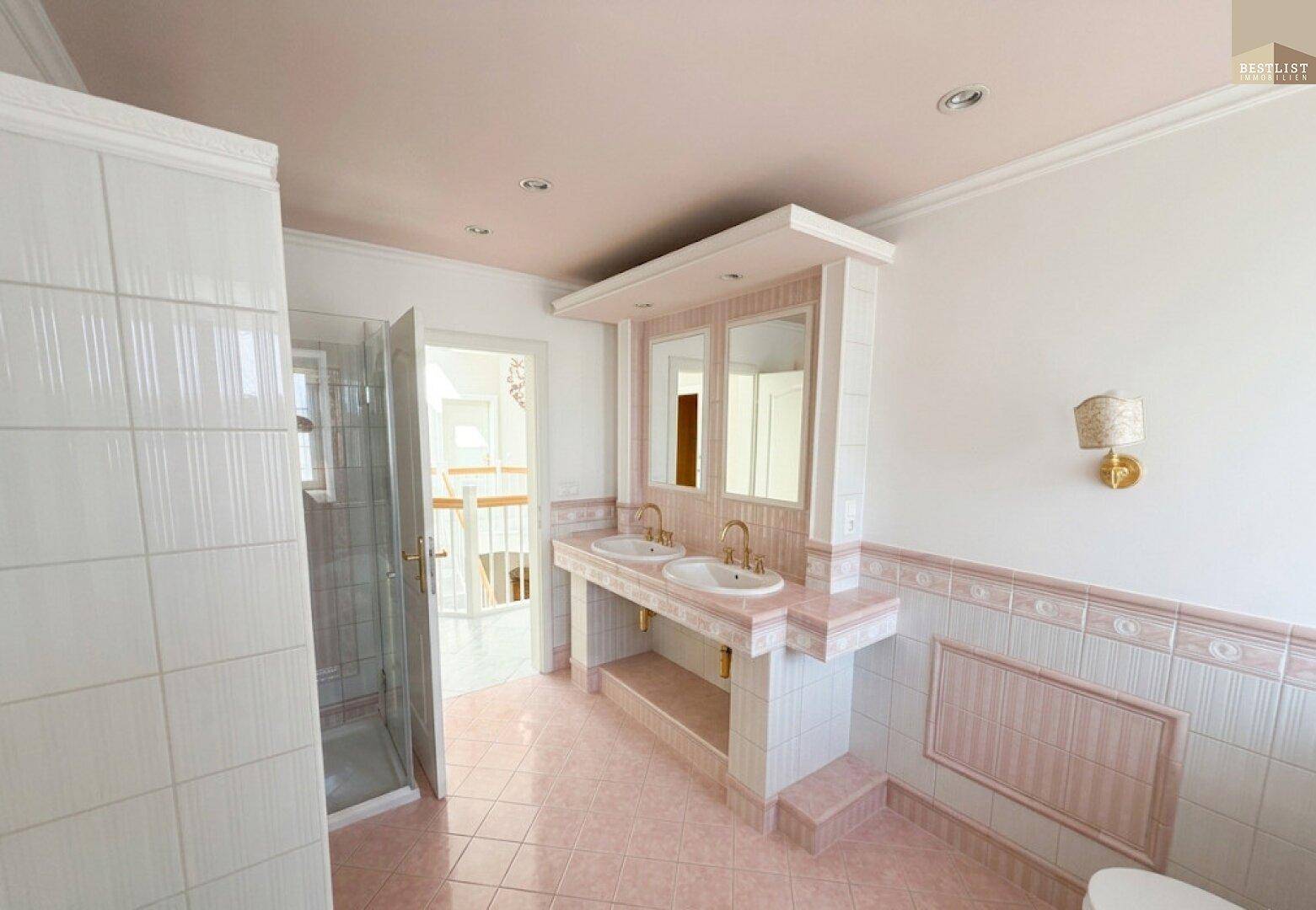 Badezimmer im 80er-Jahre-Stil mit rosa Fliesen, Doppelwaschbecken und Duschkabine.