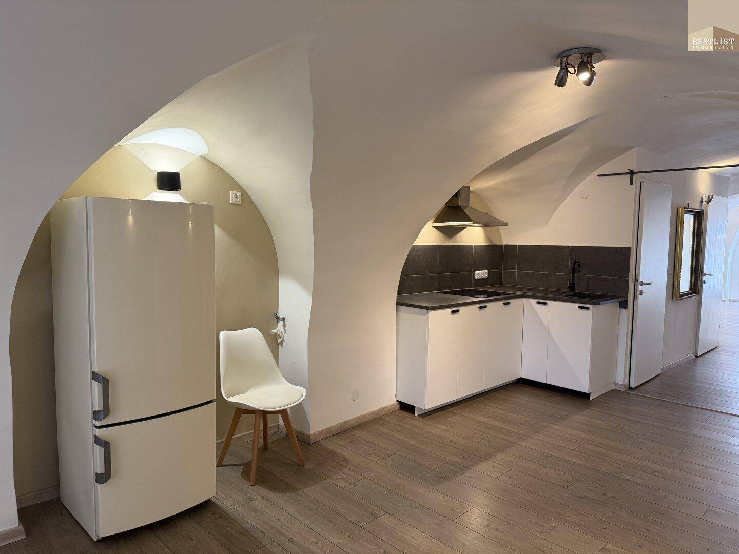 Kleine, moderne Küchenzeile unter einer Gewölbedecke mit weißem Kühlschrank.