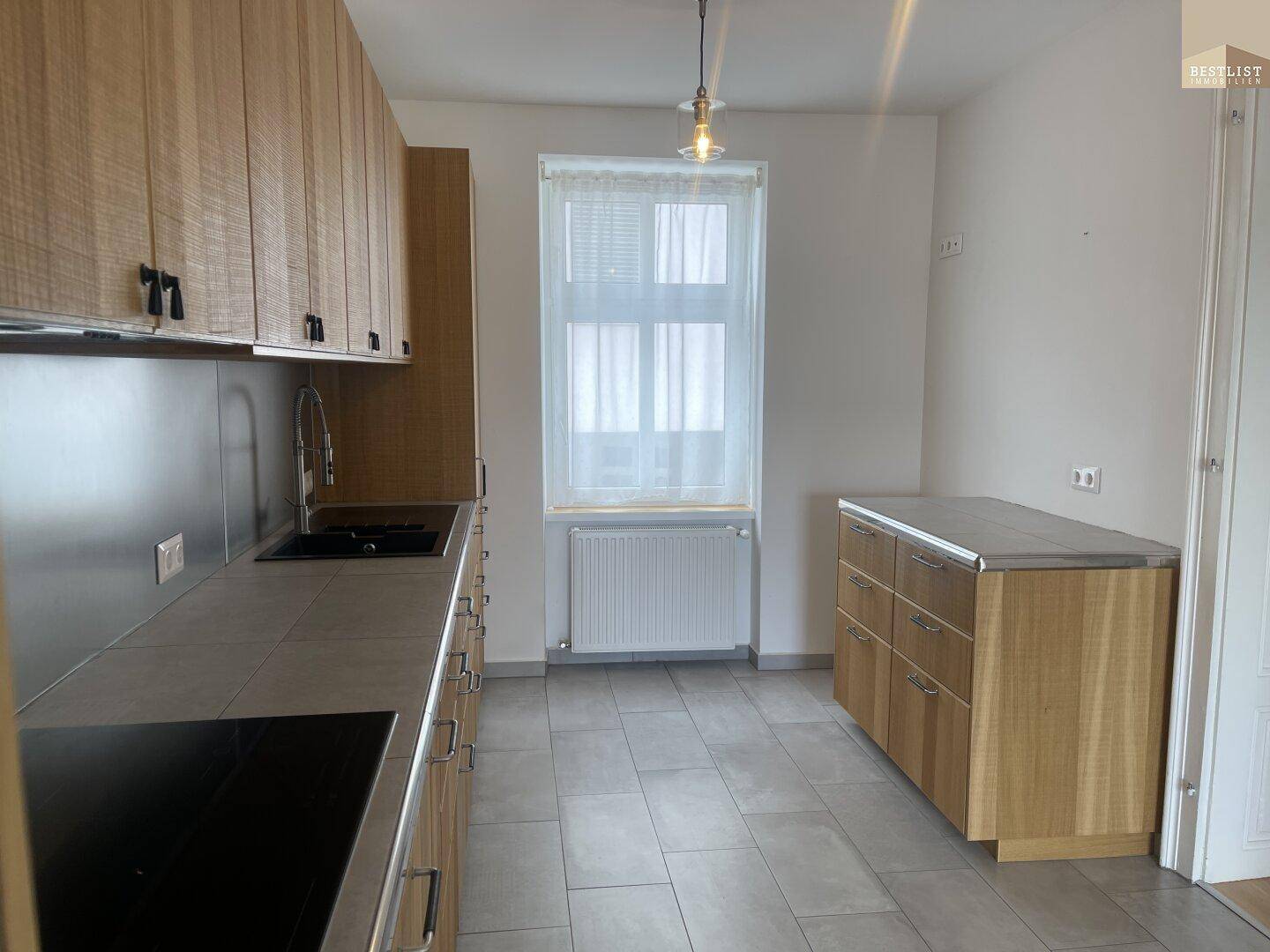 Moderne Küche mit hellen Holzschränken, Fliesenboden und einem Fenster.