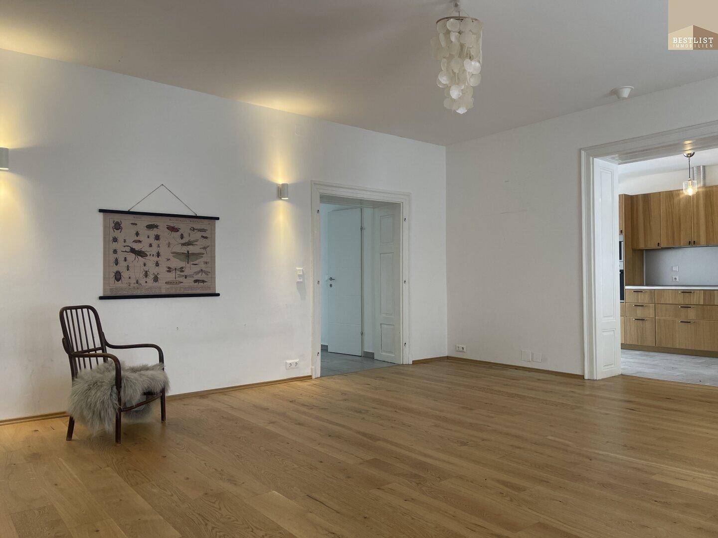 Geräumiges Wohnzimmer mit Holzboden, weiß gestrichenen Wänden und einem Holzsessel.