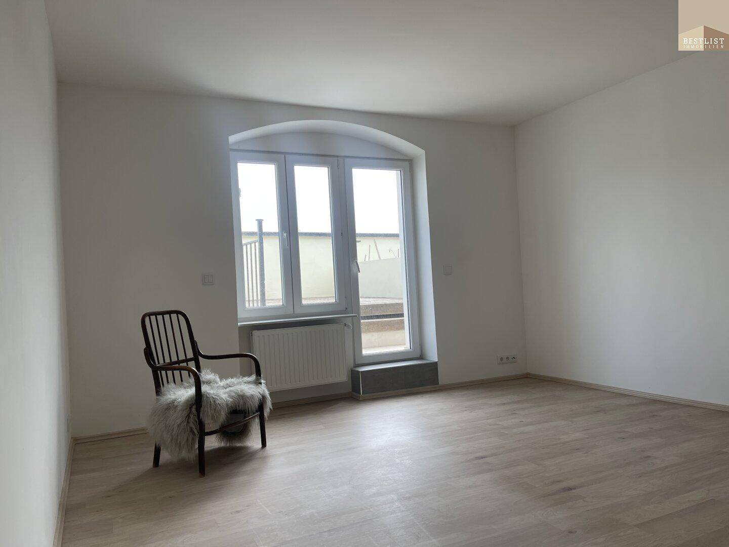 Leeres Zimmer mit einem großen Bogenfenster und hellem Holzfußboden.
