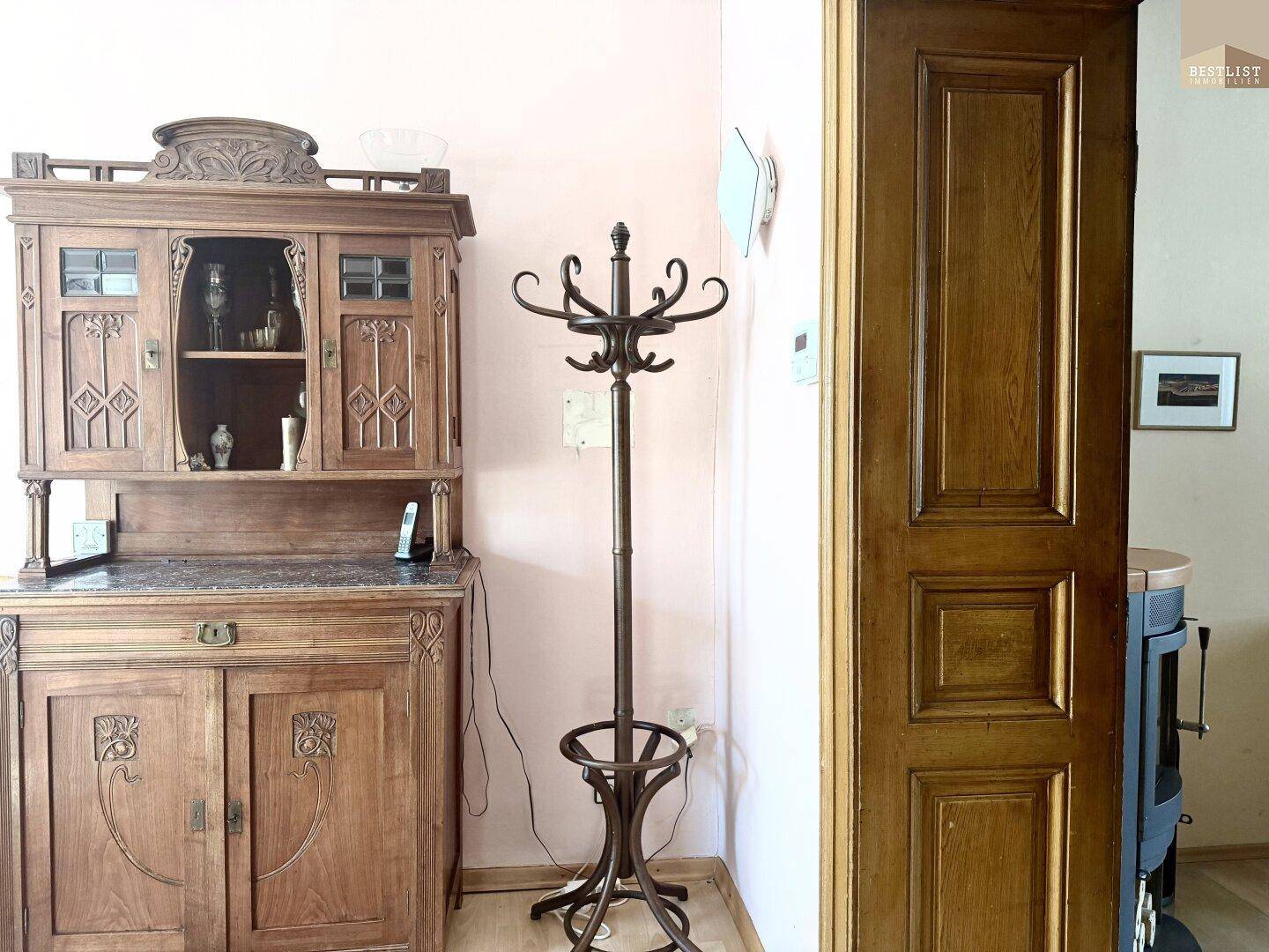 Antiker Holzschrank und Garderobenständer in einem Eingangsbereich mit Holztür.