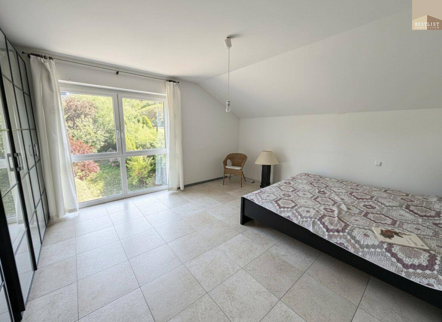 Helles Schlafzimmer mit großem Fenster, das viel Tageslicht hereinlässt und Blick ins Grüne bietet.