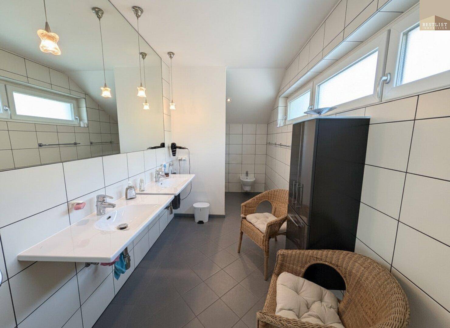 Geräumiges Badezimmer mit Doppelwaschbecken, Fliesen und Dachfenstern für natürliches Licht.