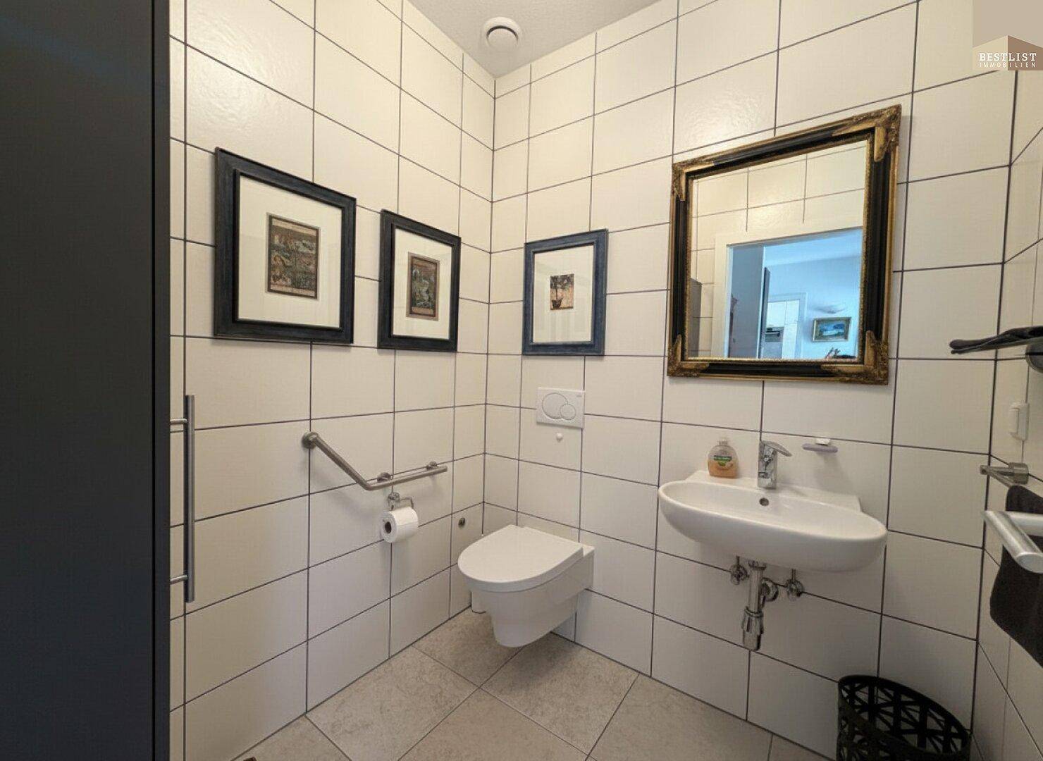 Gäste-WC mit Wand-WC, kleinem Waschbecken und Haltegriffen für Barrierefreiheit.