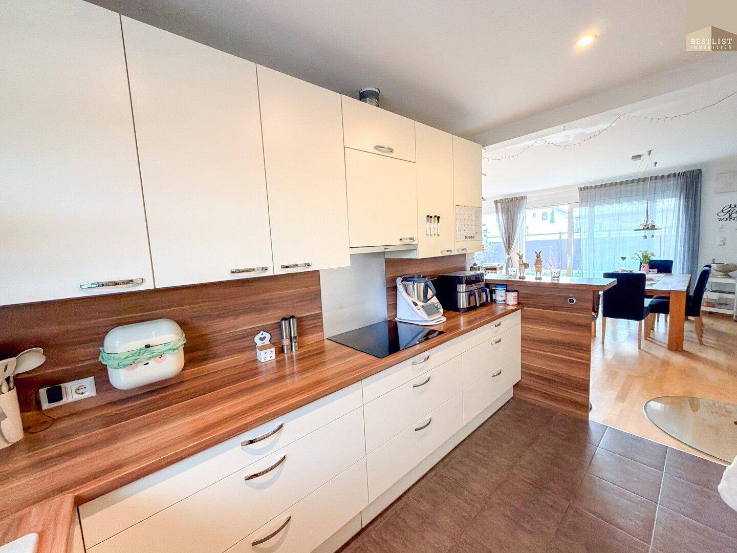 Moderne Küche mit weißen Schränken, Holz-Arbeitsplatten und Induktionskochfeld, offen zum Essbereich.
