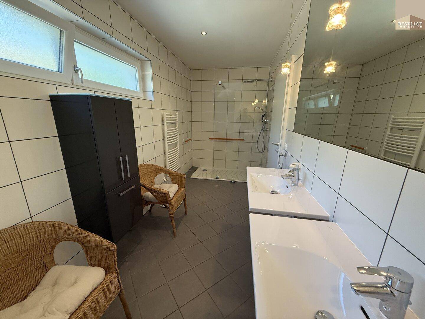 Modernes Badezimmer mit Doppelwaschbecken, großer Dusche und viel Tageslicht.