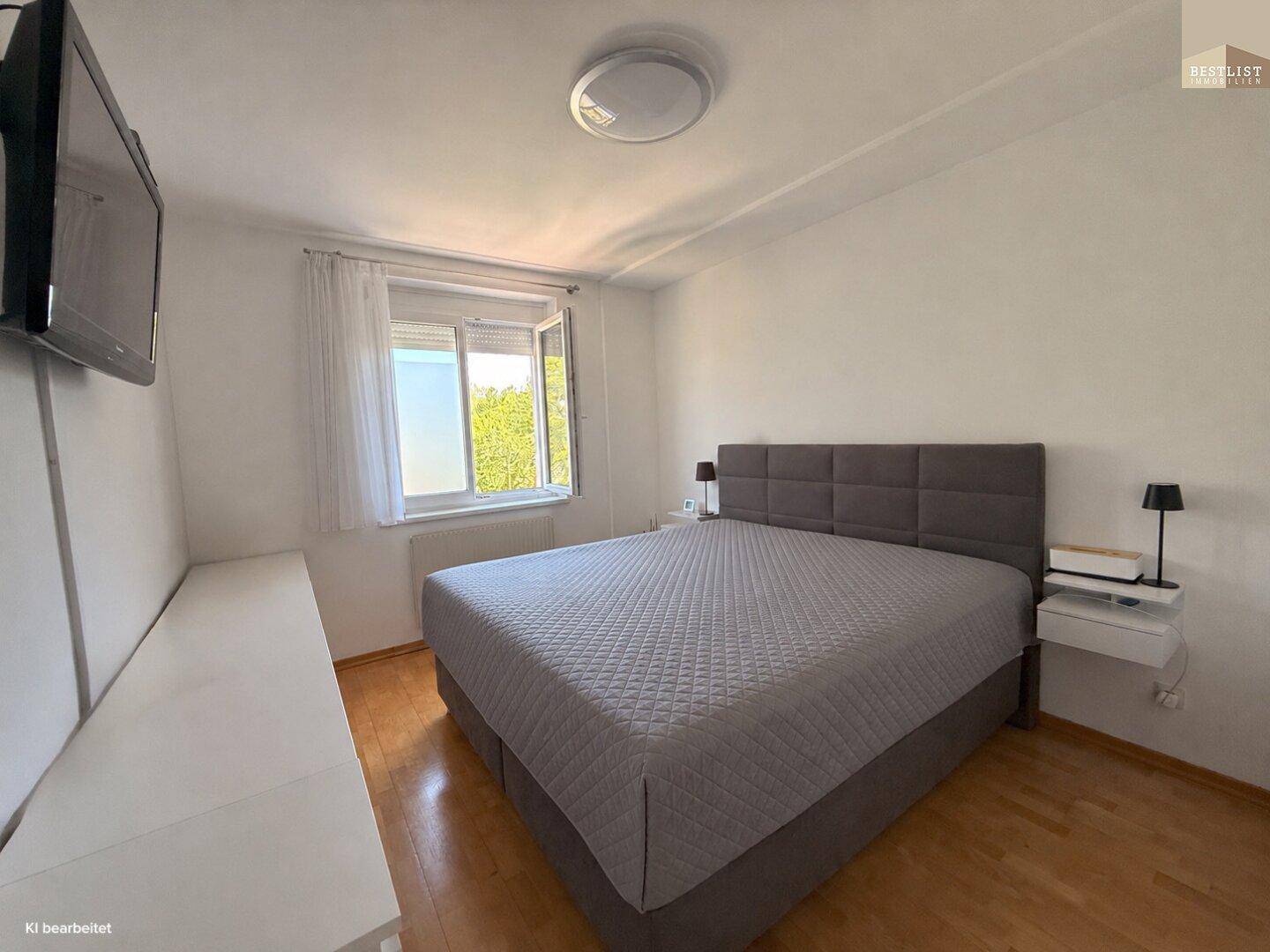 Helles Schlafzimmer mit großem Doppelbett, Parkettboden und Fenster mit Blick ins Grüne.