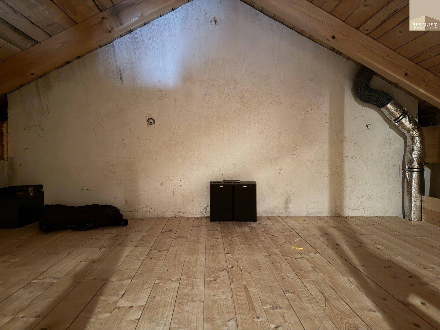 Geräumiger Dachboden mit Holzdielenboden, sichtbaren Holzbalken und einer schrägen Wand.