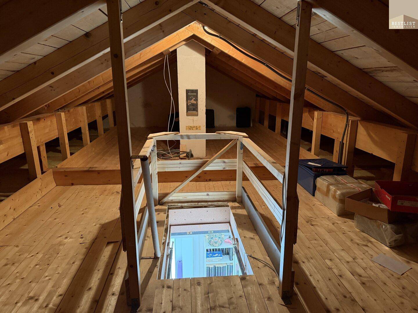 Dachboden mit Zugangsluke zum darunterliegenden Stockwerk und sichtbarer Holzkonstruktion.