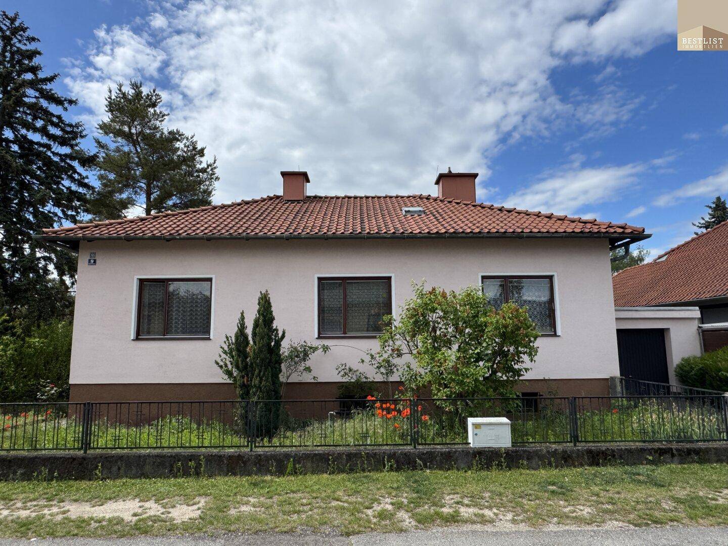 Frontale Ansicht des Einfamilienhauses mit rosa Fassade, braunem Sockel und klassischem Ziegeldach.